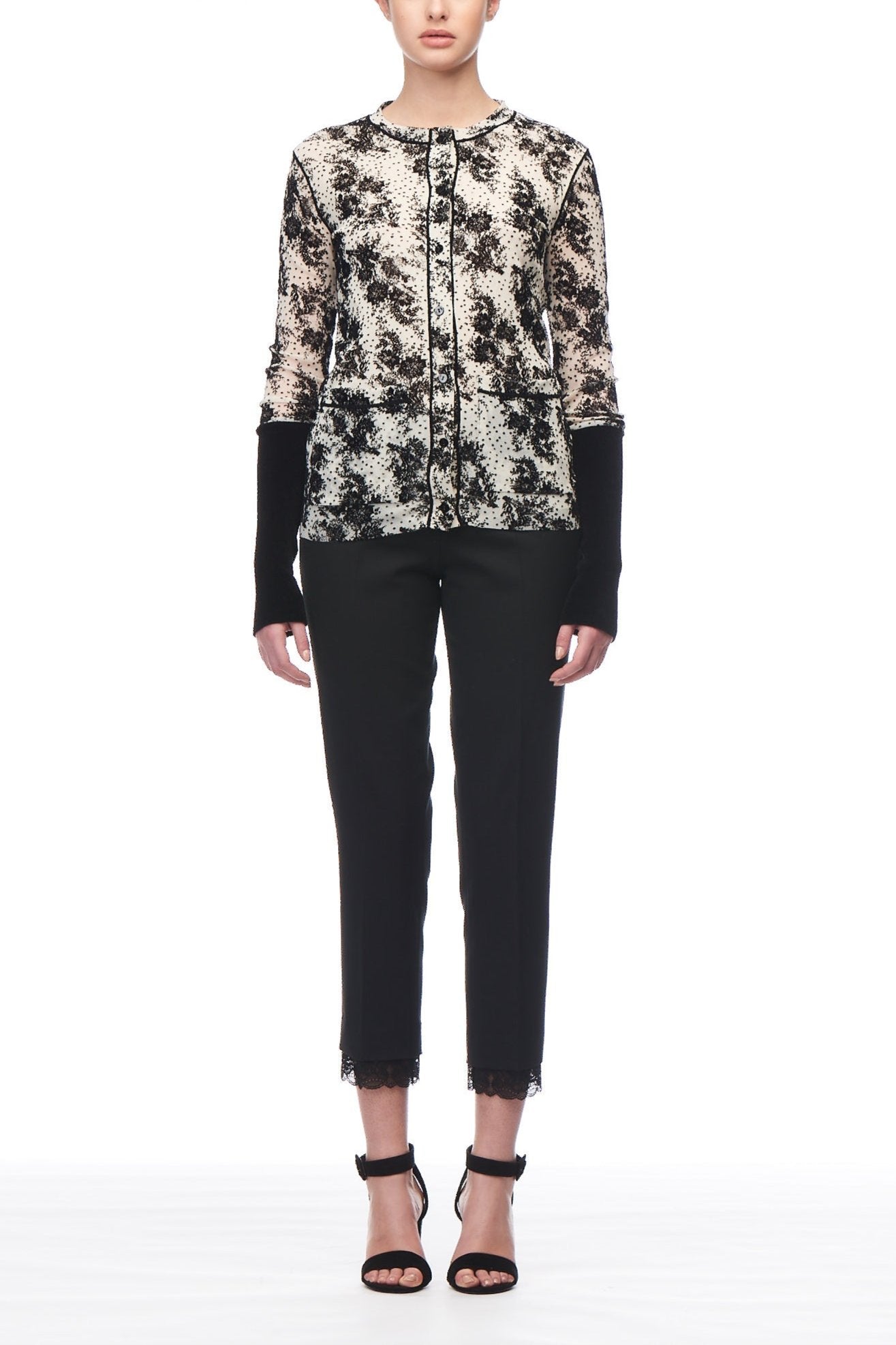 A model showcasing the Fuzzi Woman Cozy Floral Cardigan, featuring a chic black and white lace pattern and a belted waist, is paired with sleek black cropped pants and strappy black heels, posed against a white backdrop.