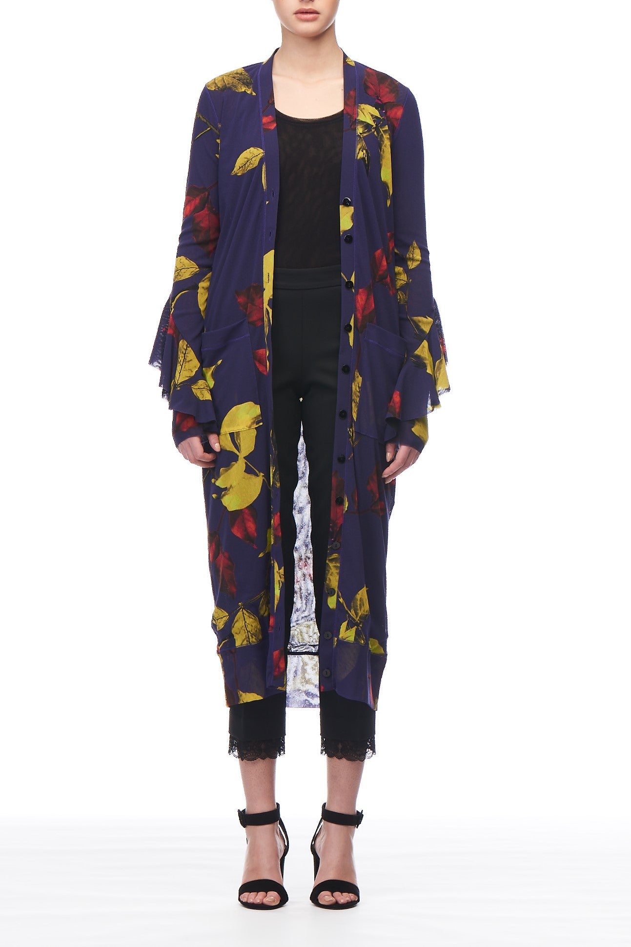 A person is styled in a Fuzzi Woman Sheer Floral Cardigan by Fuzzi, featuring a long, vintage design with a V-neckline and adorned with vivid yellow and red floral patterns. The cardigan is paired over a black lace top and dark pants. Black high-heeled sandals complete the look, set against a plain white background.