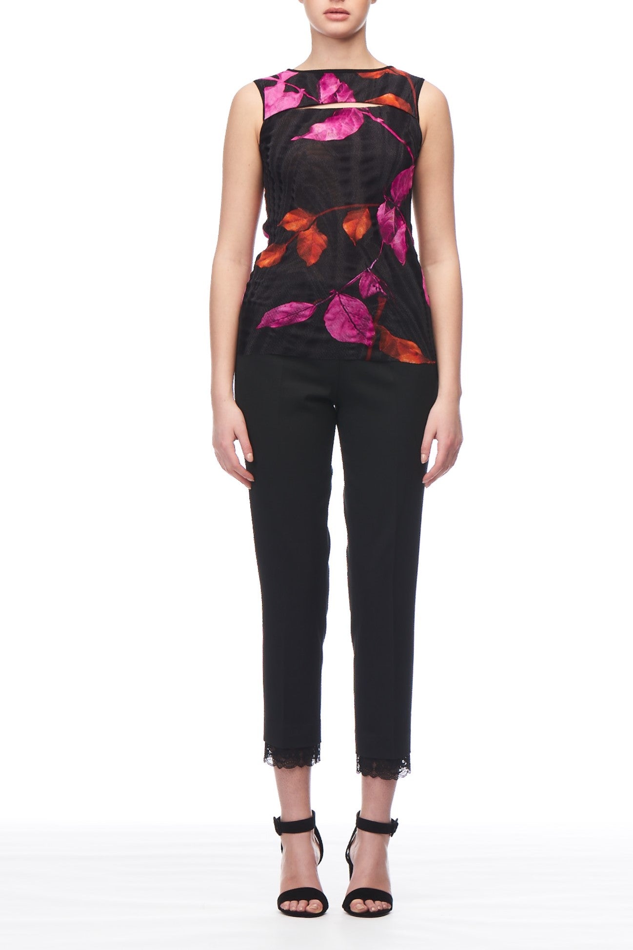 Someone is dressed in a Fuzzi Woman Floral Mesh Top, a vintage sleeveless black piece featuring pink and orange floral print, paired with black pants. The outfit is completed with black high-heeled sandals against a plain white background.