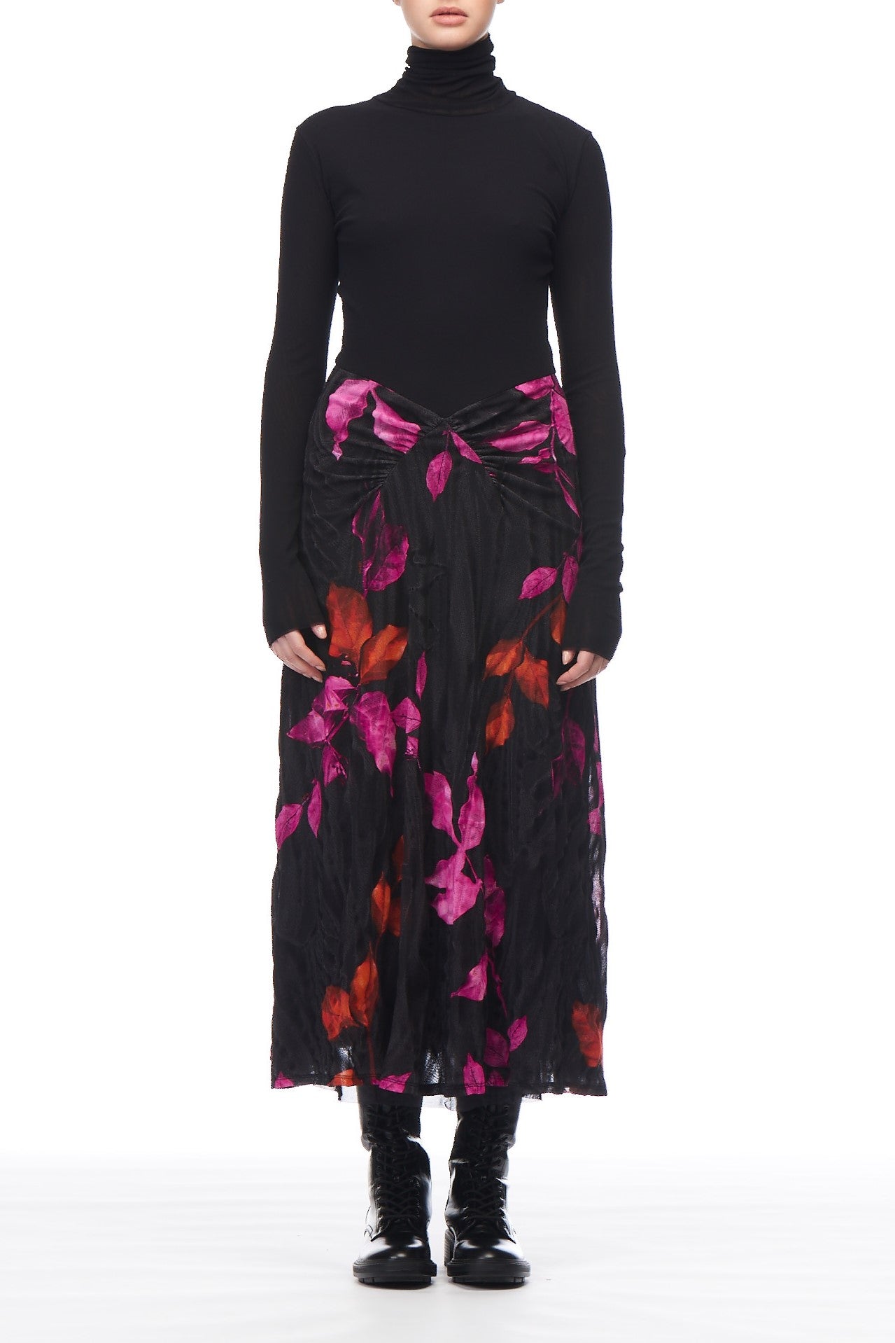 A person is wearing the Fuzzi Woman Long-Sleeve Dress, featuring a long black skirt with striking pink and red floral prints. They have paired the dress with edgy black boots. The scene is set against a plain white background, and the person's face is not visible.