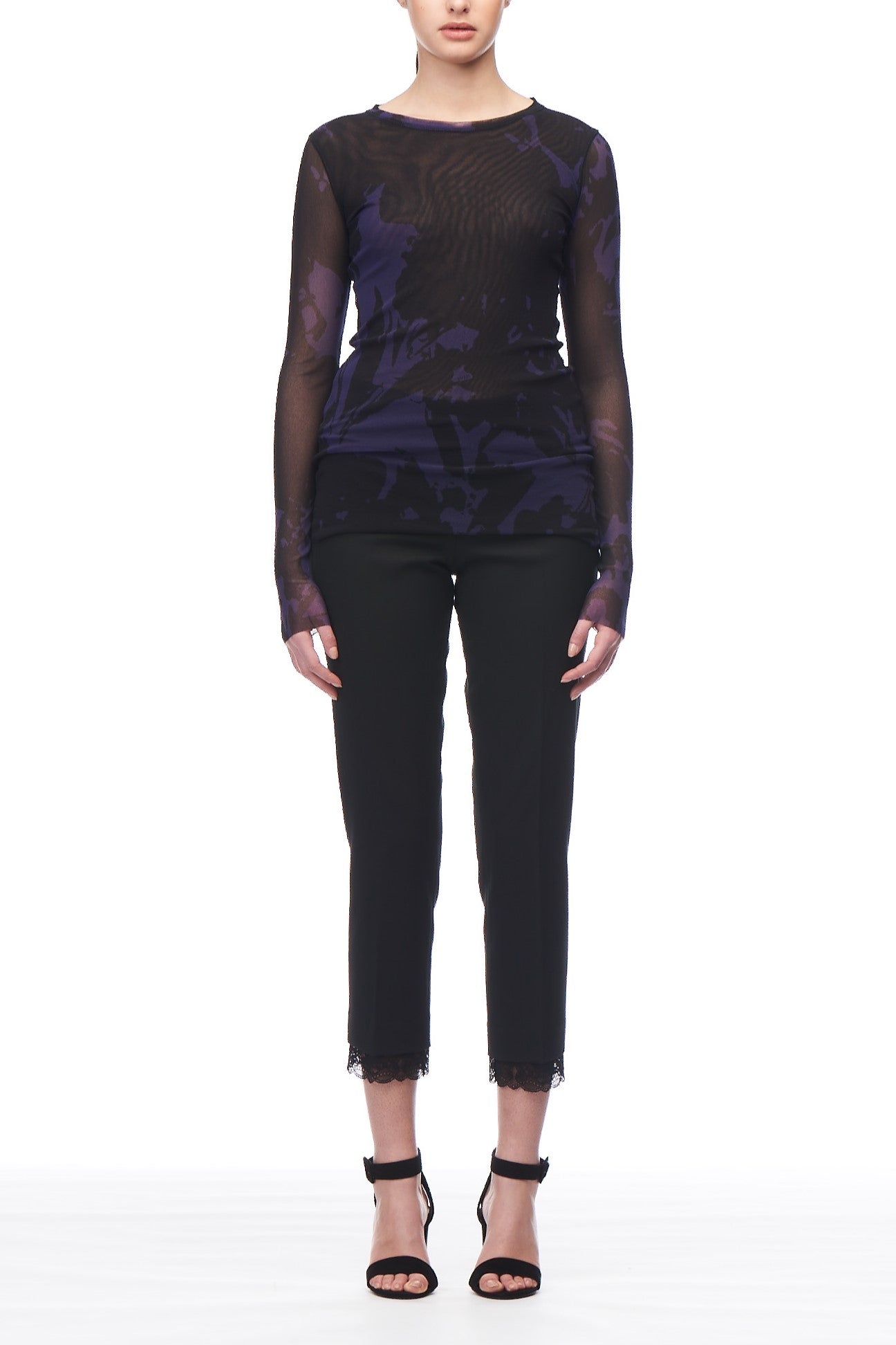 A person wearing the Fuzzi Woman Mesh Top in a stylish, long-sleeved, semi-sheer black and purple design paired with black pants. The pants boast a vintage lace trim at the hem. They are complemented by black high-heeled sandals while standing against a plain white background.