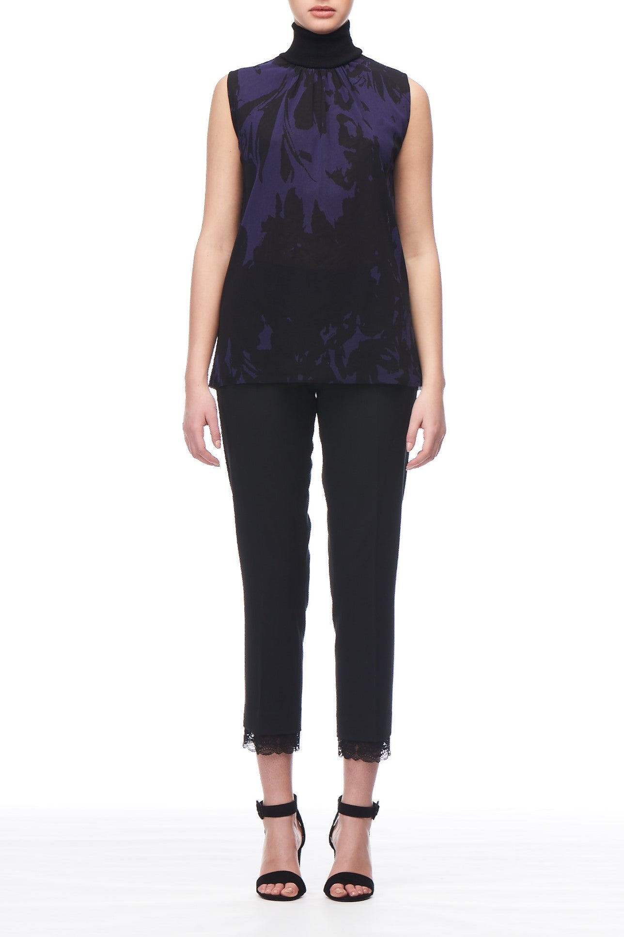 A person is wearing a Fuzzi Woman Abstract Print Sleeveless Top in navy floral and black cropped pants with a lace hem, paired with sheer black high-heeled sandals, standing against a plain white background.