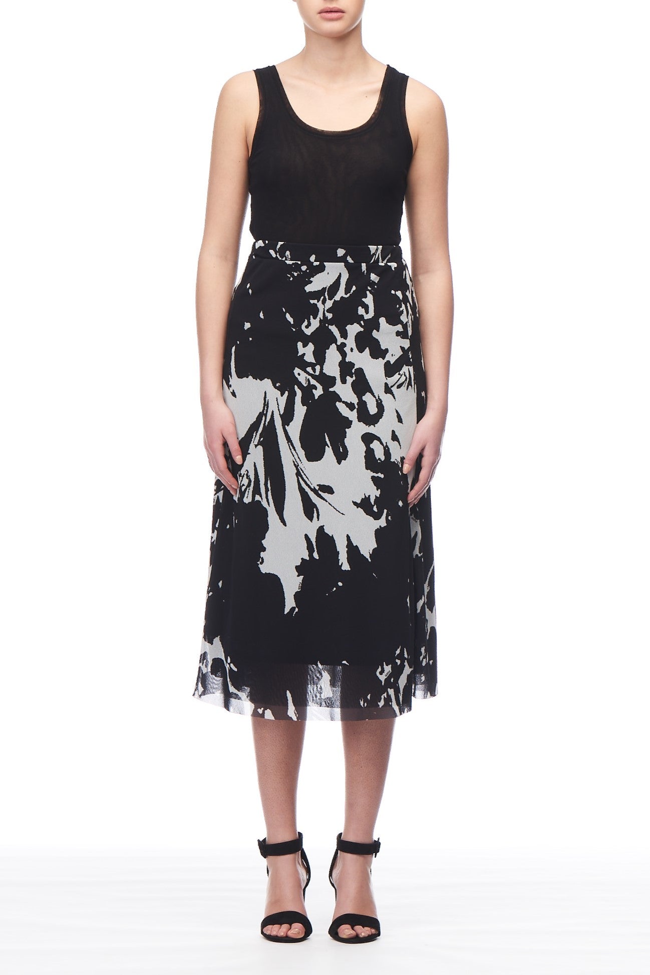 A person wearing a sleeveless black top and the Fuzzi Woman Abstract Art Skirt from Fuzzi stands against a plain white background. They complement the outfit with black high-heeled sandals, adding an element of sophistication to the ensemble.