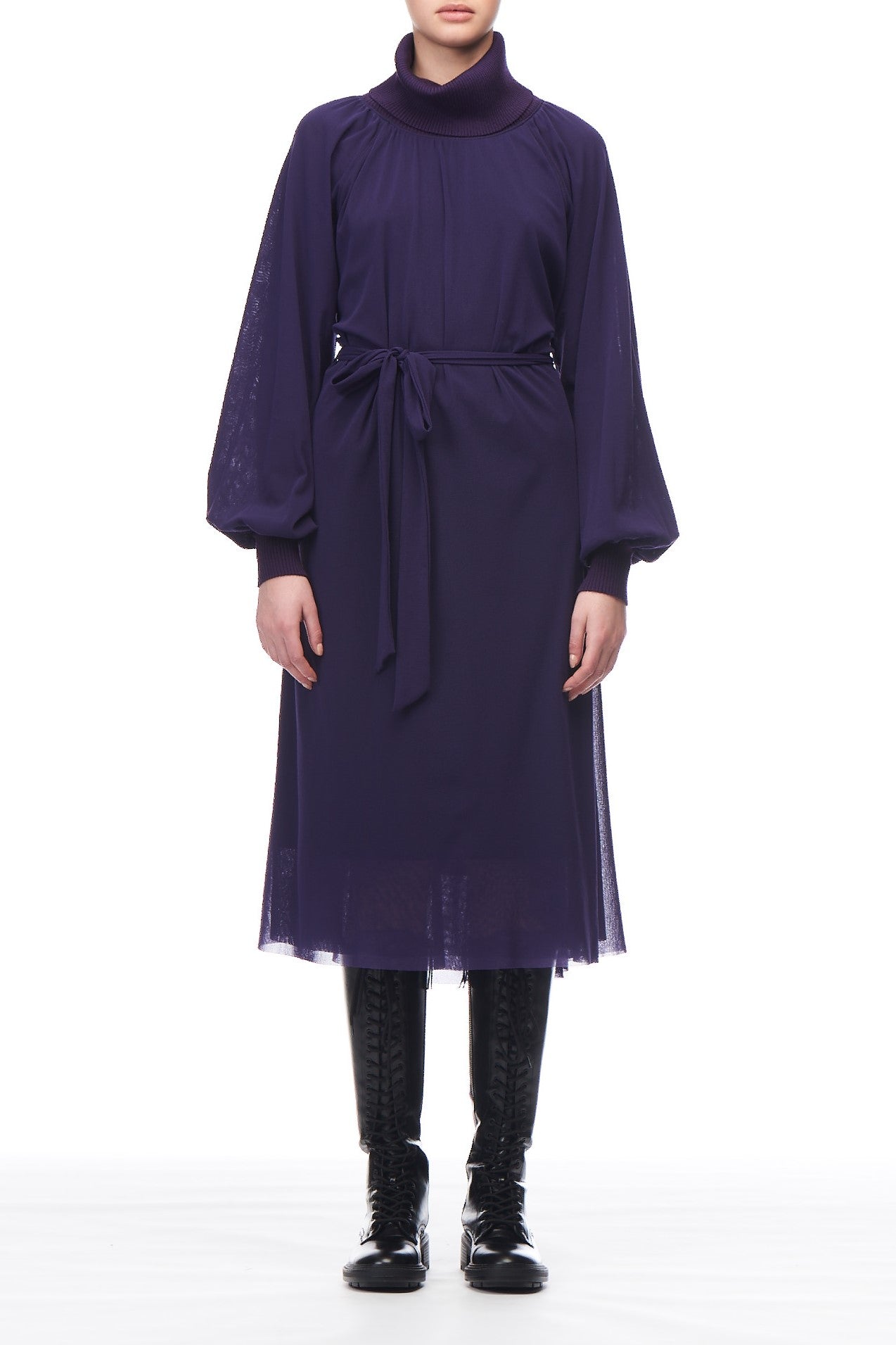 A person wearing the Fuzzi Woman Timeless Dress, a long dark purple design by Fuzzi, features a high collar and waist tie with sheer fabric and long, loose sleeves. The asymmetrical hemline pairs elegantly with black lace-up boots against a plain white background.