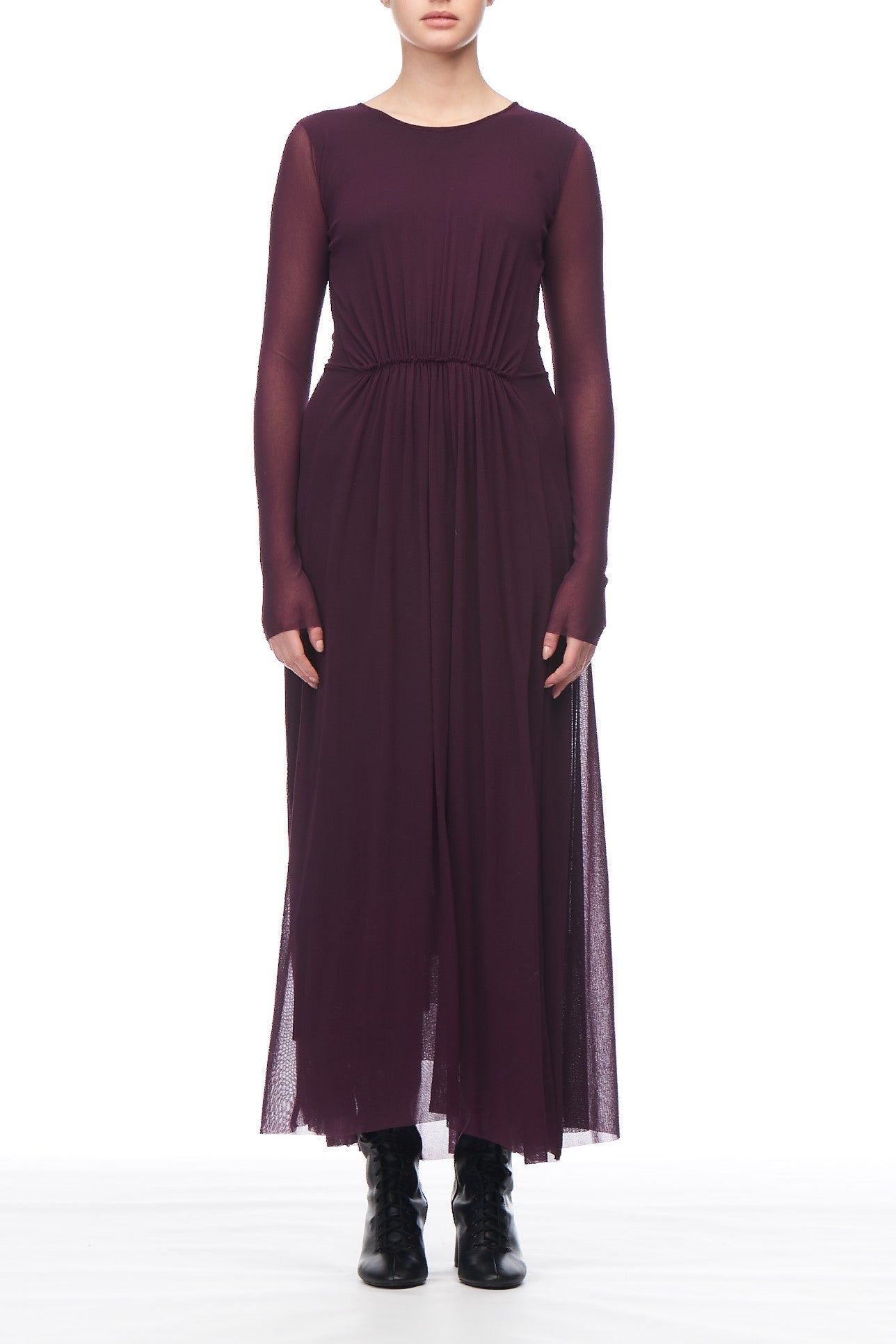 A person wearing the Fuzzi Woman Sheer Maxi Dress, a long-sleeved, floor-length elegant purple dress by Fuzzi, stands against a white background. The vintage dress features a sheer overlay and is paired with black ankle boots, though the person's face remains unseen.