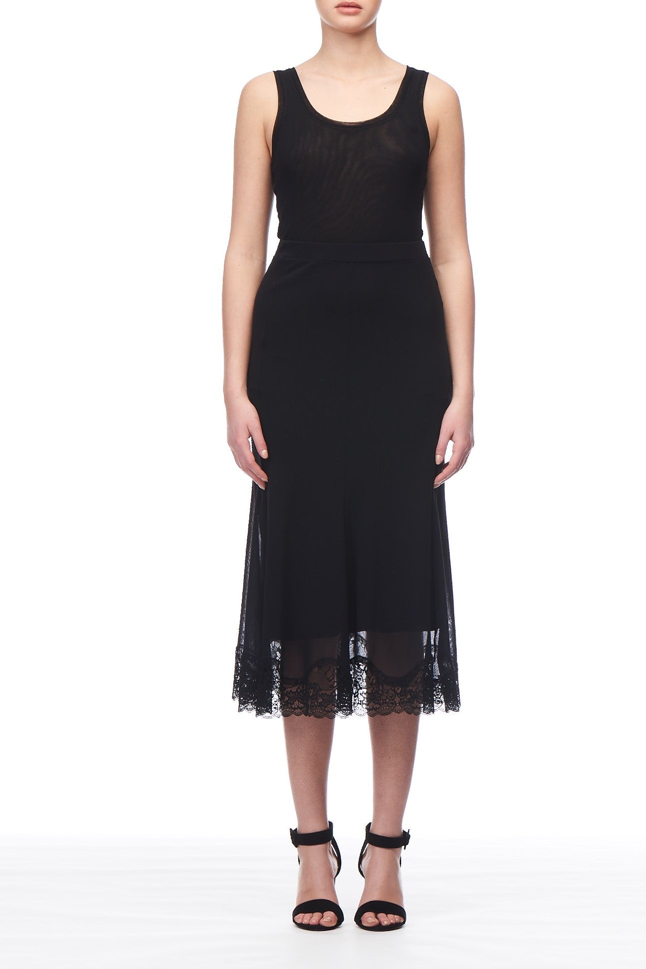 A person wearing the Fuzzi Woman Black Lace Trim Midi Skirt, which features delicate floral motifs, stands against a white background. They pair it perfectly with black strappy high-heeled sandals.