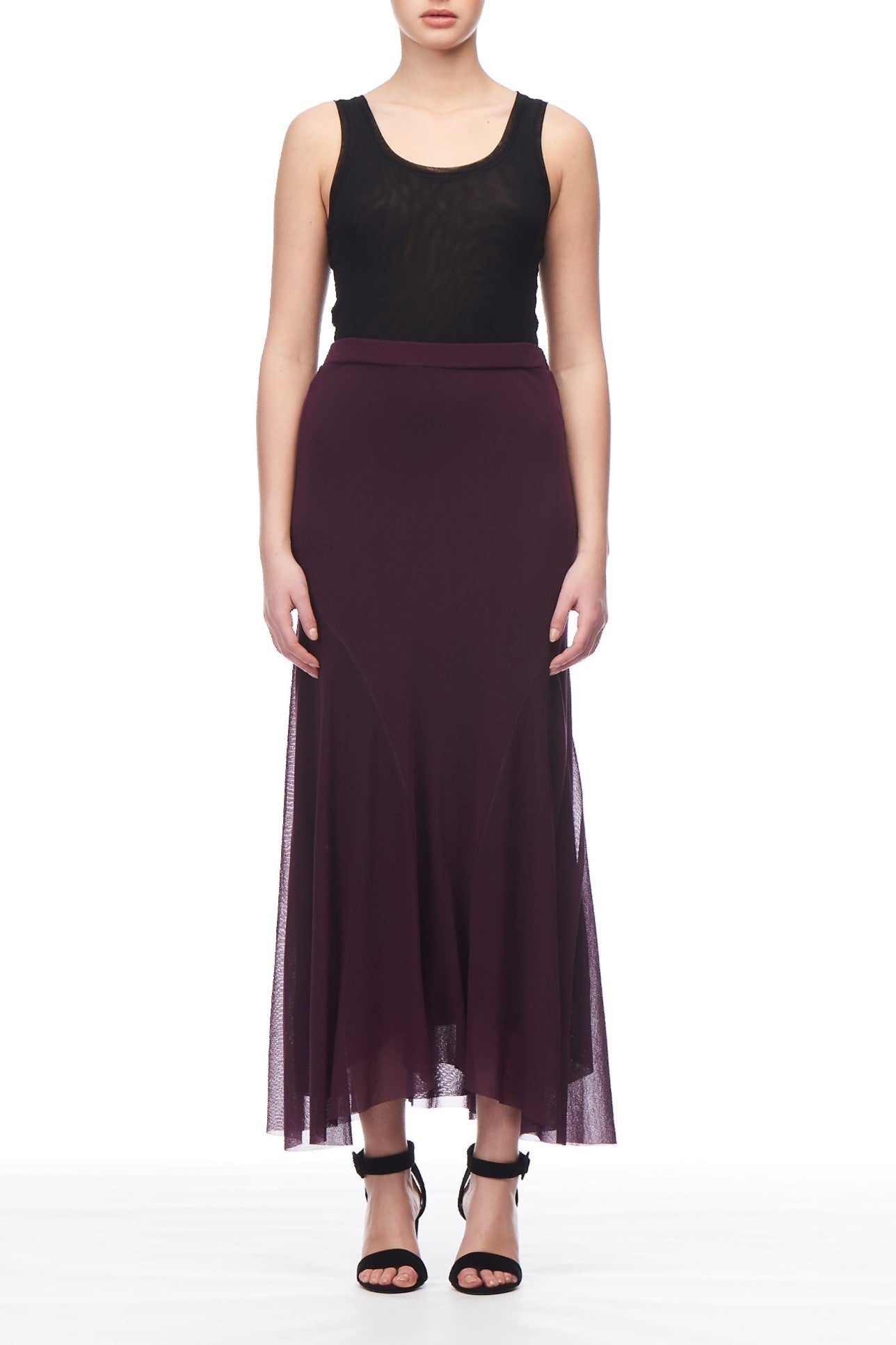 A person stands wearing a sleeveless black top and the Fuzzi Woman Pleated Midi Skirt, featuring a flowing dark purple color with an A-line silhouette, reaching the ankles. They are also wearing black open-toed heels against a plain white background.