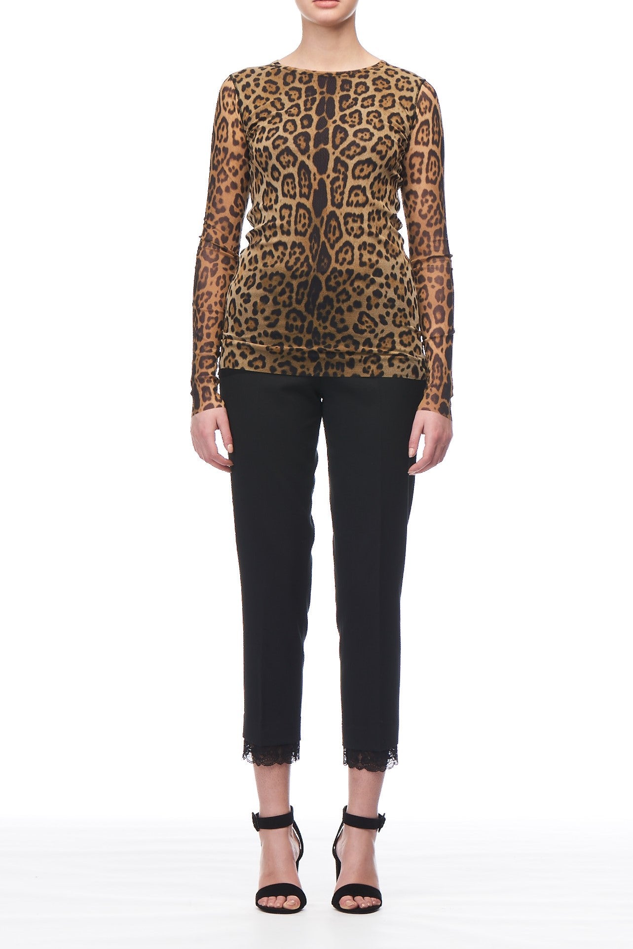 A person wearing the Fuzzi Woman Leopard Print Mesh Long Sleeve Top and black cropped pants with lace trim, paired with black high-heeled sandals, showcases a vintage piece. The white background highlights this wardrobe essential's bold style and unique flair.