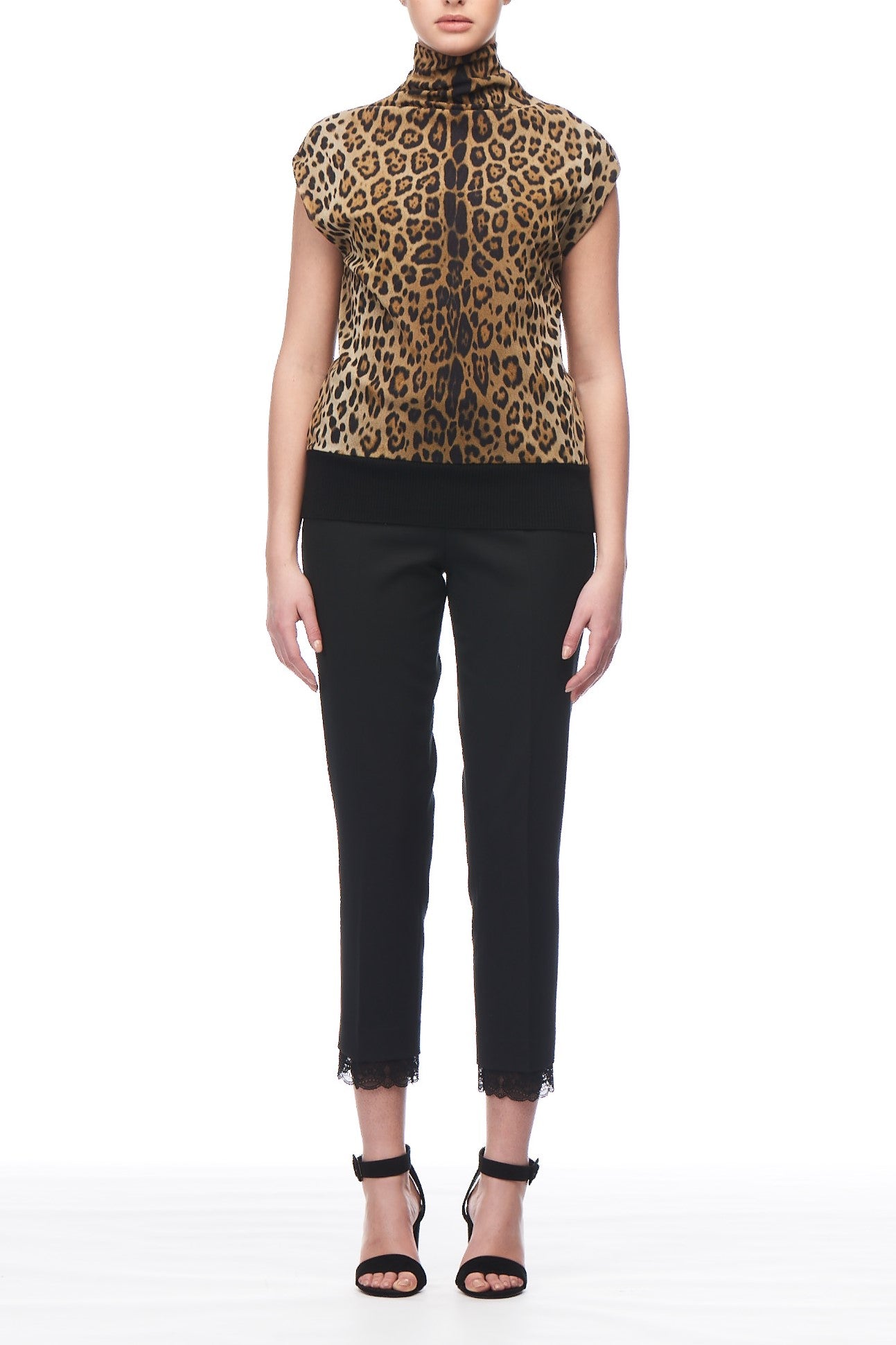 A person stands against a white background wearing the Fuzzi Woman Leopard Print Neck Top and black cropped pants. This vintage-inspired outfit is paired with chic black high-heeled sandals.