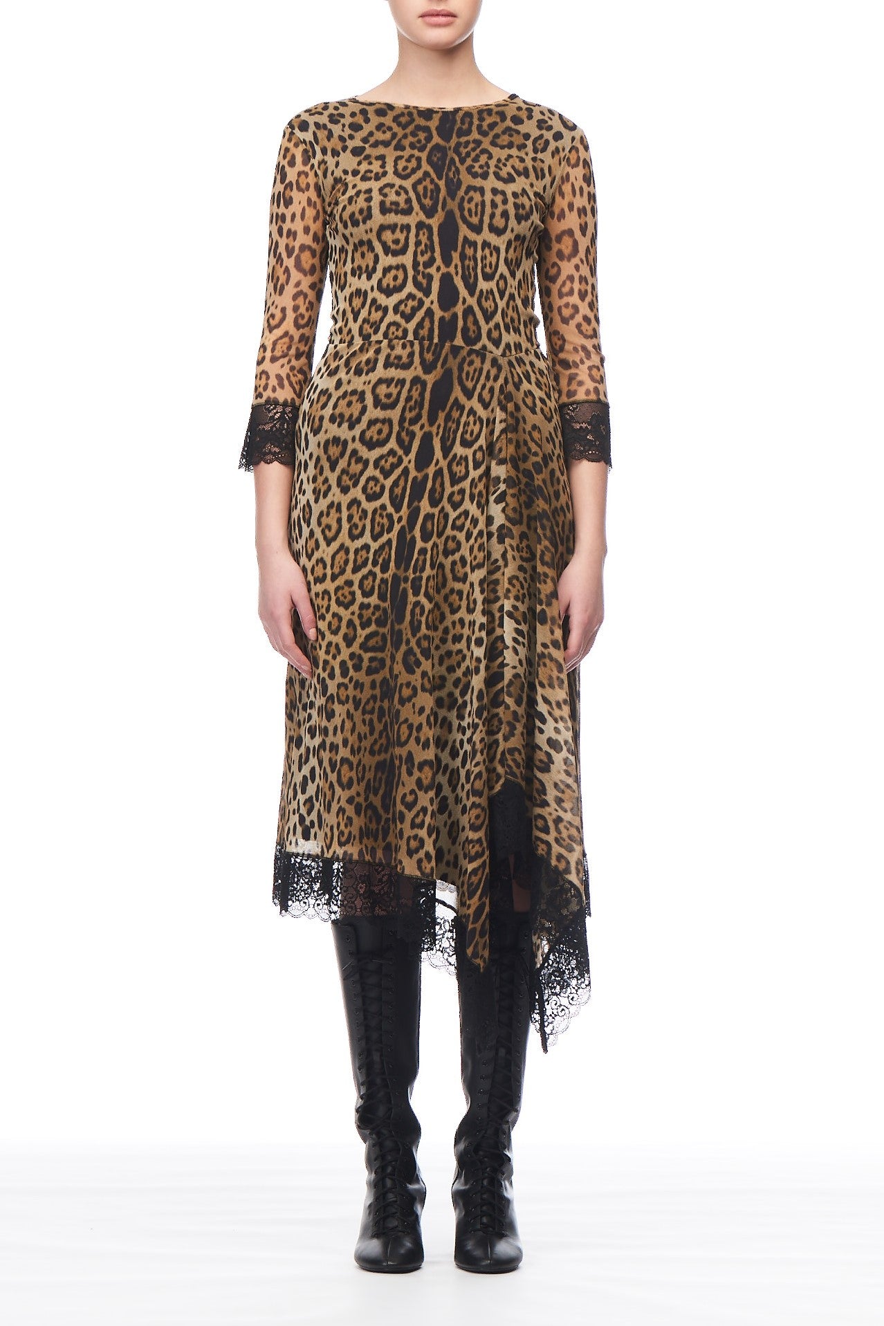 A person wearing a vintage piece—a Fuzzi Woman Leopard Dress with Lace Trim. This knee-length dress, from the brand Fuzzi, features an asymmetrical hemline and black lace trim on the sleeves and hem. Paired with knee-high black lace-up boots, they stand elegantly against a white background.