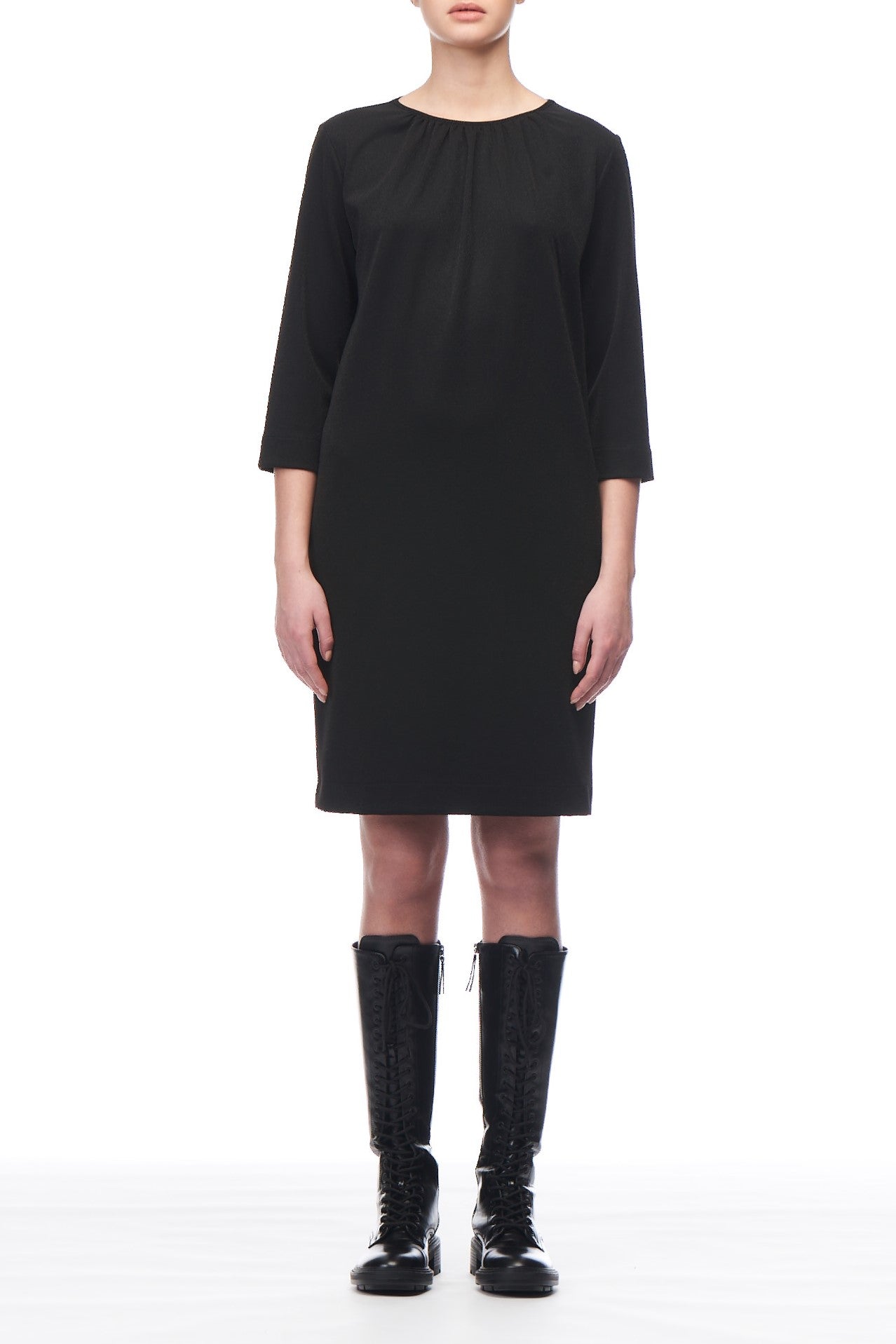 A person is standing against a white background, wearing a knee-length Fuzzi Woman Relaxed Fit 3/4 Sleeve Dress, which features an asymmetrical hemline. They are paired with black knee-high lace-up boots. The image does not show their head as it is cropped above the shoulders.