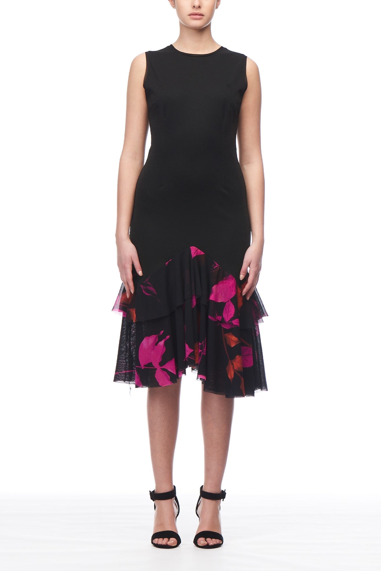 Wearing the Fuzzi Woman Ruffled Hem Floral Print Dress, which boasts a sleeveless black design adorned with purple and pink floral patterns, a person radiates vintage elegance. Paired with black high-heeled sandals, this ensemble offers versatile styling against the simple white backdrop.