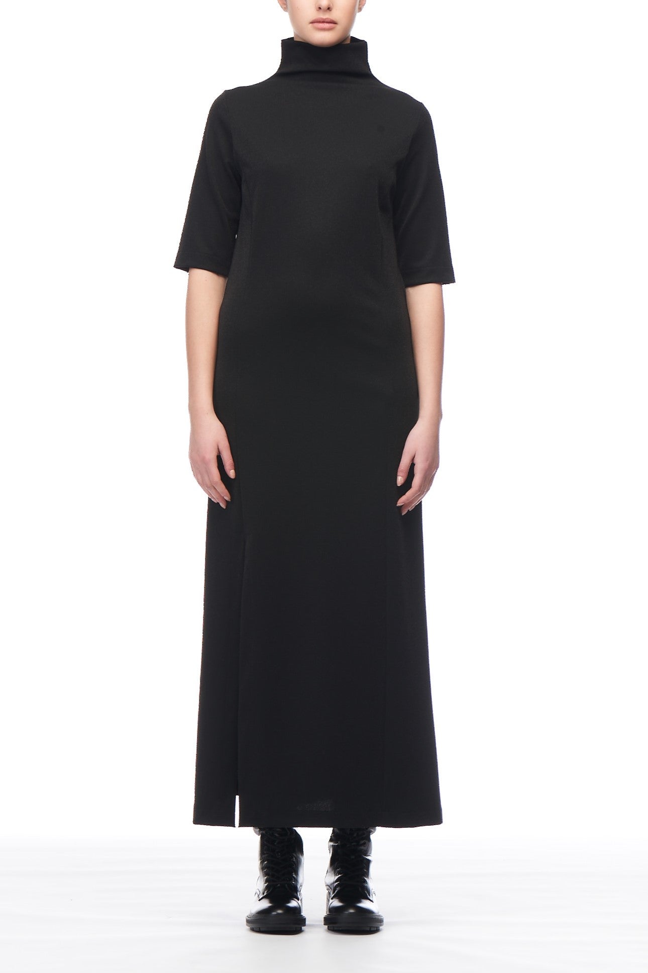 The individual is dressed in a chic, ankle-length Fuzzi Woman Turtleneck Midi Dress with short sleeves, paired with black boots. Positioned against a plain white backdrop, they face forward, radiating an effortlessly elegant vibe that echoes the allure of a timeless vintage style.