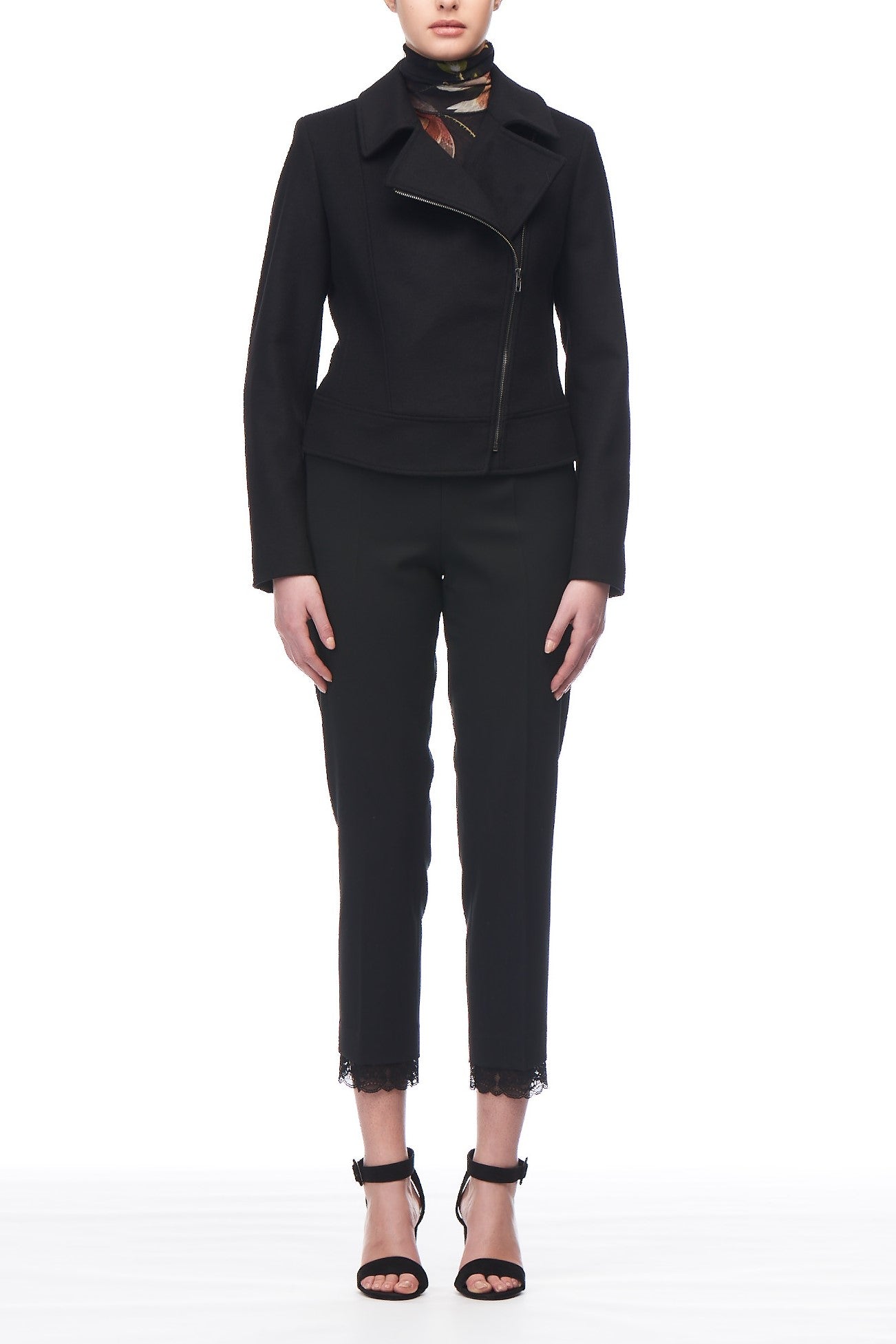 Against a white background, a person wears a stylish Fuzzi Woman Black Jacket featuring an asymmetrical zip, complements them with black pants that have lace trim at the hems and black strappy heels. Their neck is adorned with a patterned scarf.