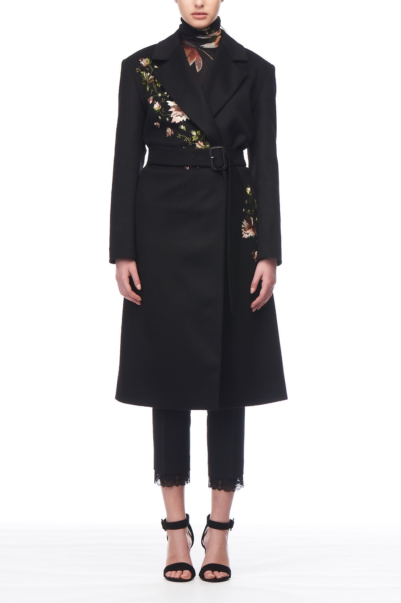 A person gracefully wearing the Fuzzi Woman Embroidered Coat by Fuzzi, which boasts sophisticated floral embroidery on the shoulder and waist, effortlessly complemented by a coordinating black turtleneck, pants, and high heel sandals with ankle straps. The simple white background perfectly highlights this vintage piece.