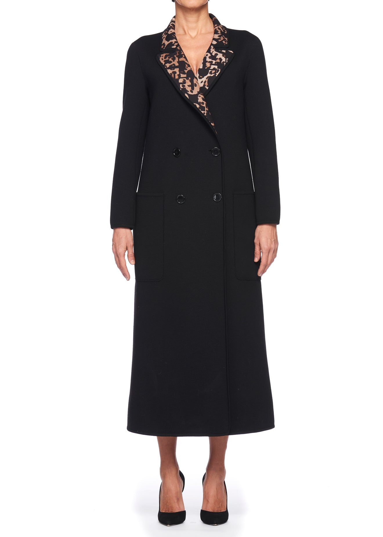 A person wearing the Fuzzi Woman Studded Double-breasted Coat in black, featuring a patterned collar and a belted waist, stands against a white background. This vintage-inspired piece, complete with two large pockets, pairs perfectly with their black heels.