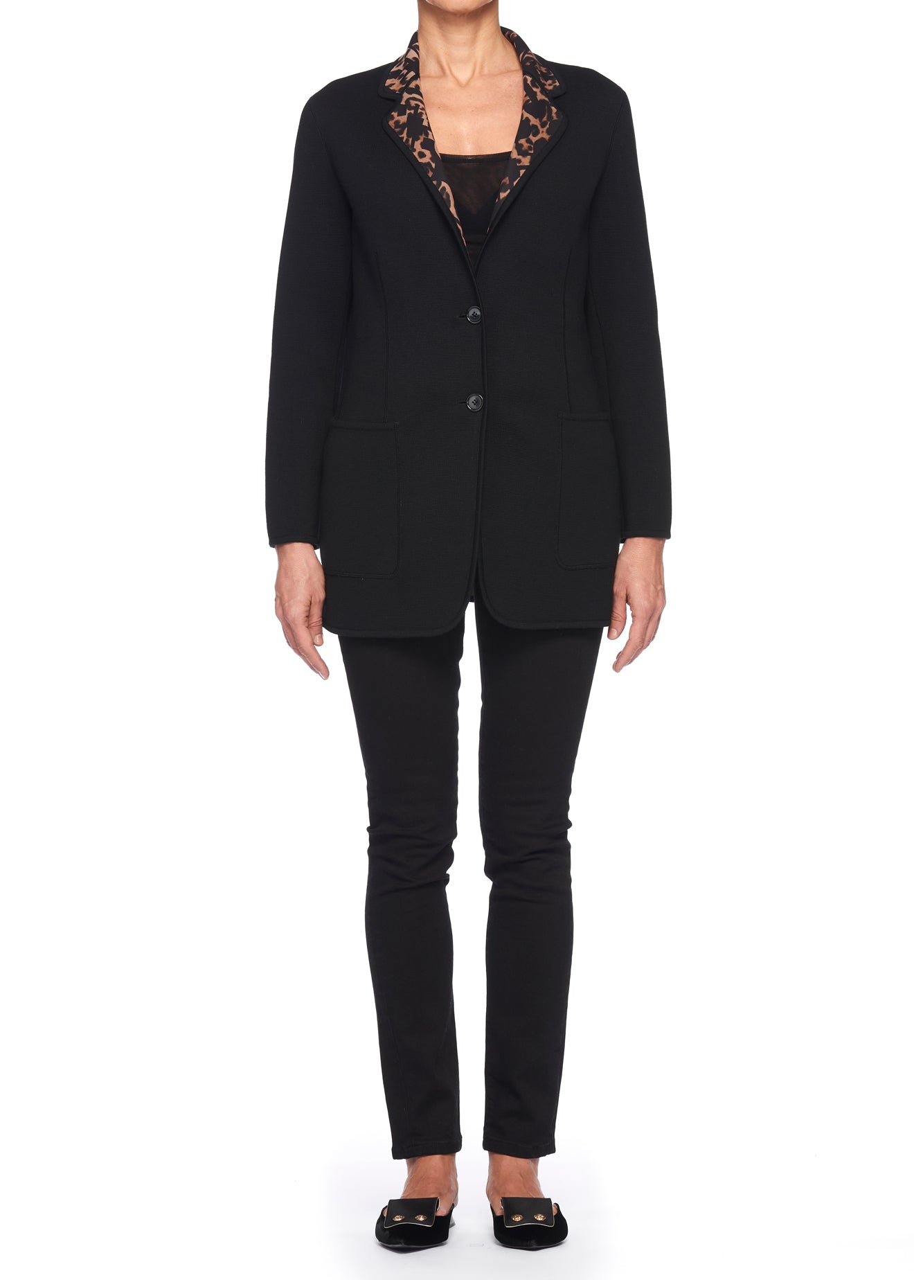 A person is wearing a Fuzzi Woman Wool Blazer, featuring vintage black wool fabric with leopard print detailing inside the collar, paired with black pants and black flats. They stand against a plain white background, exuding timeless elegance.