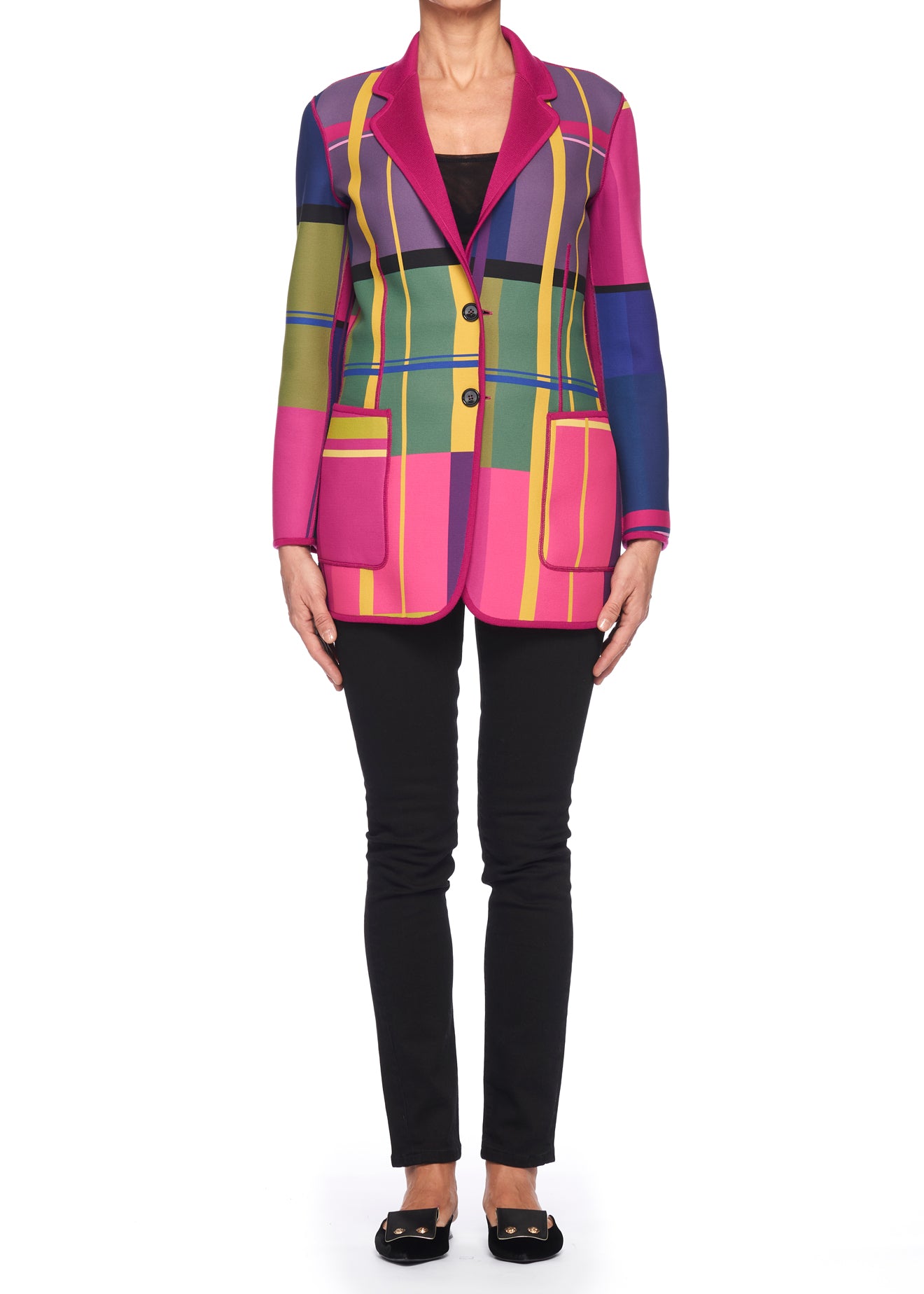 An individual stands against a plain white background, wearing the Fuzzi Woman Reversible Wool Blazer by Fuzzi, featuring vibrant multicolored plaid patterns of pink, green, and blue over a black top. They pair it with black pants and flat shoes.