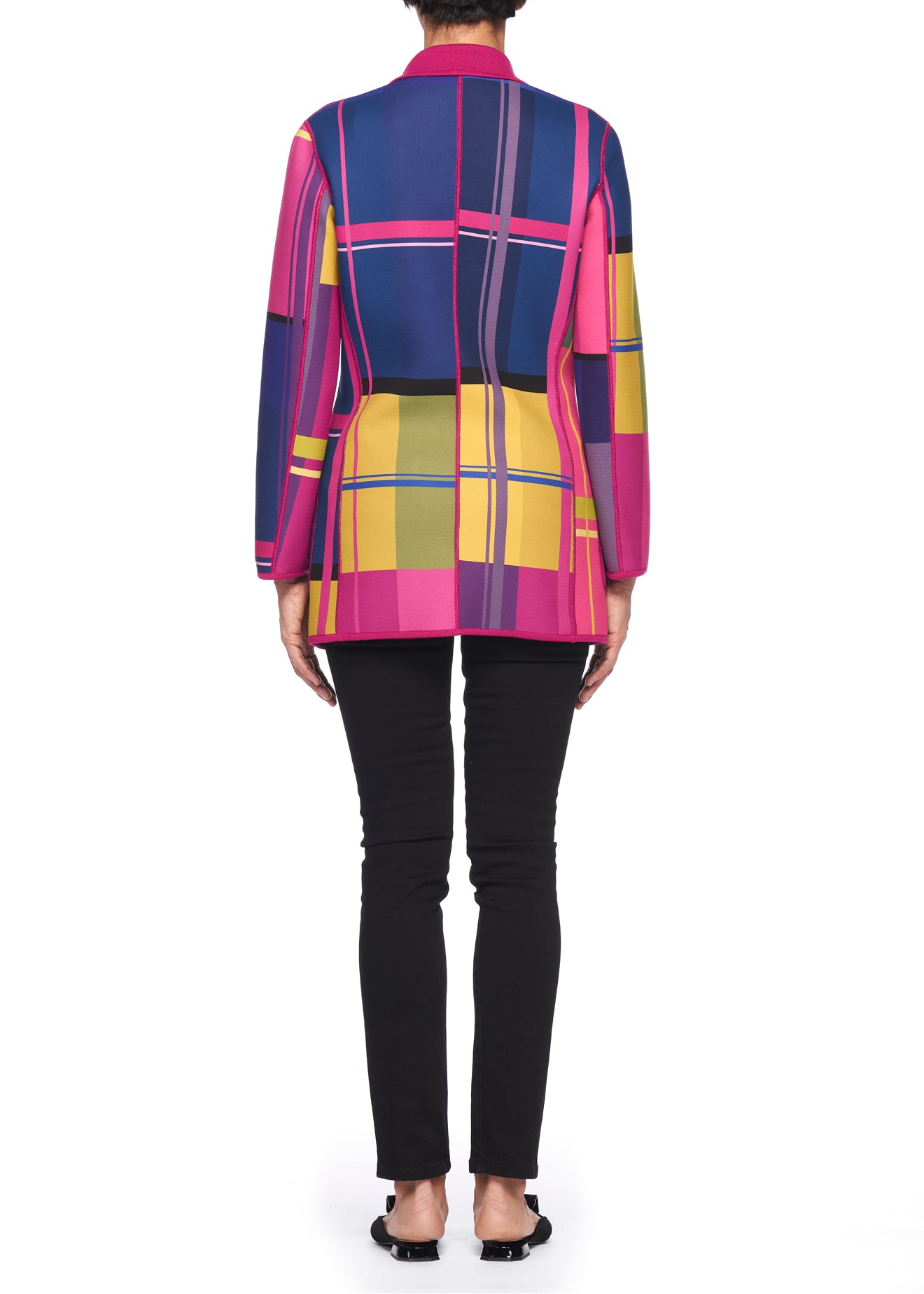 A person stands facing away, highlighting the reversible design of the Fuzzi Woman Reversible Wool Blazer, which features a long-sleeve top in a vibrant plaid pattern of pink, blue, yellow, and green. The ensemble includes black pants and flat shoes against a plain white background.