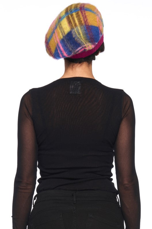 A person facing away, wearing a black sheer long-sleeve top and the Fuzzi Woman Tartan Beanie, featuring a colorful pattern in shades of yellow, pink, and blue. The background is plain white.