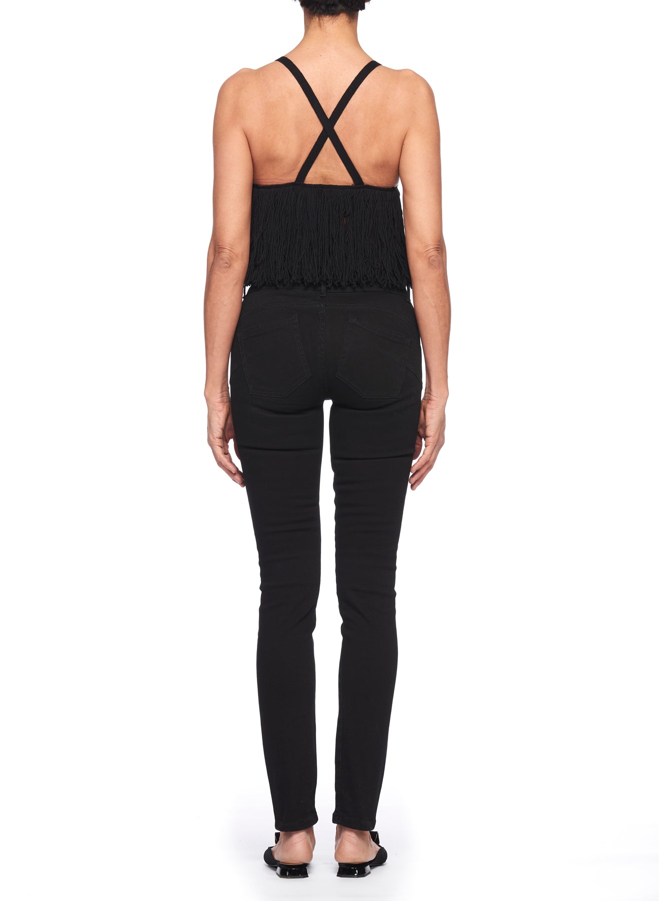 A person is shown from the back wearing a Fuzzi Woman Sleeveless Top with crisscross straps and a fitted silhouette, paired with black skinny jeans. Standing against a white background, they have their hair tied back in a sleek style and are barefoot, embodying an effortlessly chic aesthetic.