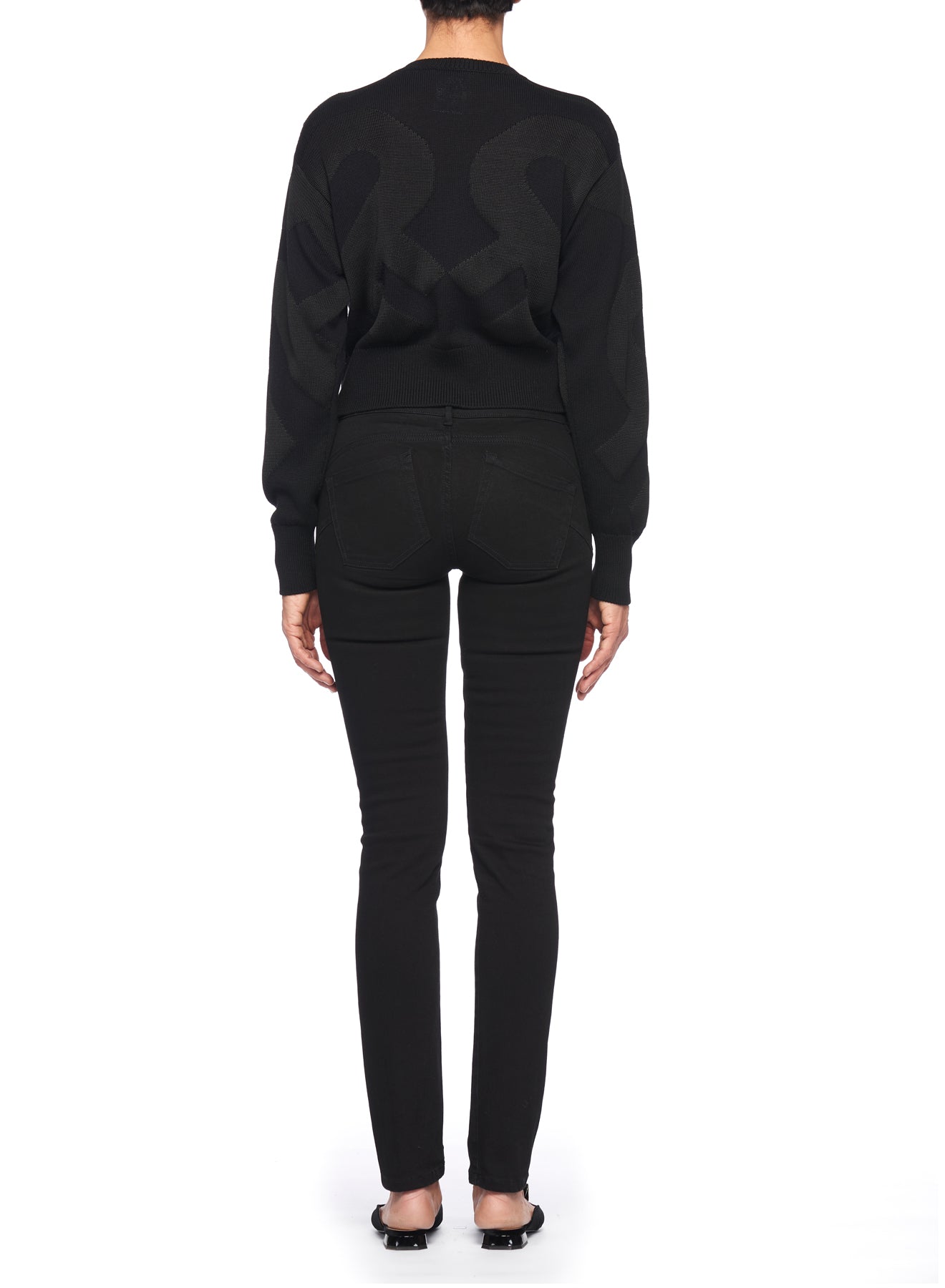 A person is seen from the back wearing a Fuzzi Woman Cropped Sweater by Fuzzi in black, paired with black pants against a white background. The oversized fit enhances the street style look, complemented by black flat shoes adorned with bows.