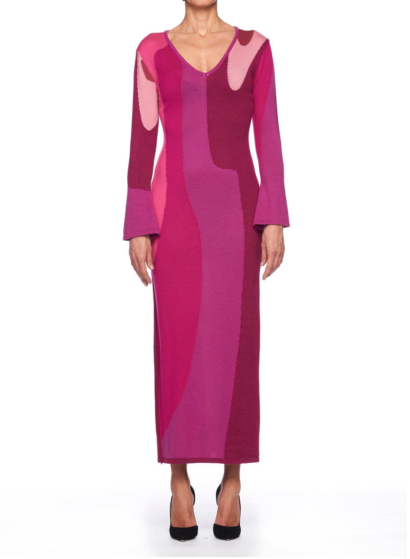 A person is wearing the Fuzzi Woman Modern Art Midi Dress, a long-sleeved, V-neck piece featuring abstract pink and purple patterns and a fitted silhouette reminiscent of modern art. The dress reaches ankle-length and is stylishly paired with black heels, set against a plain white background.