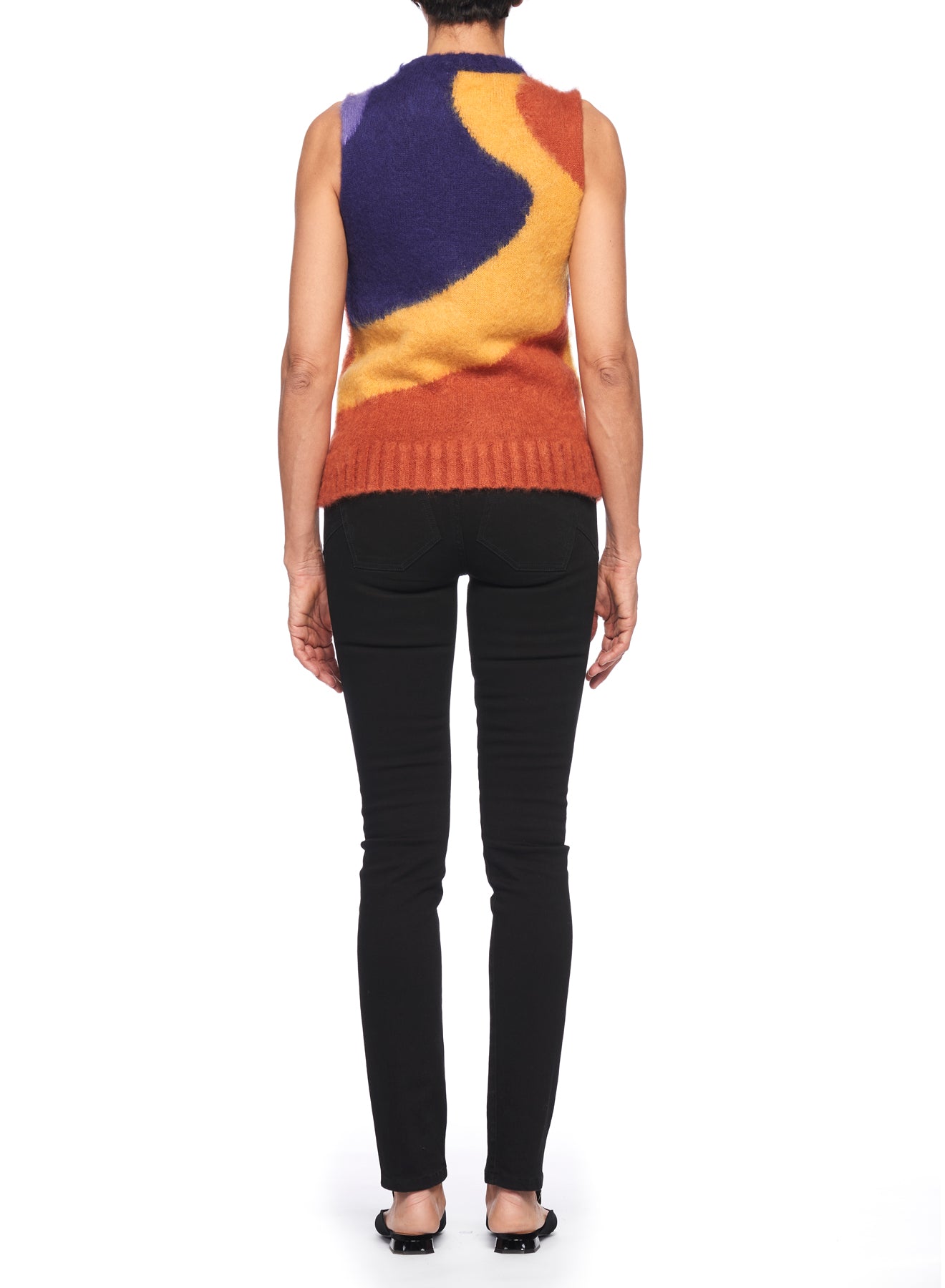 A person is shown from behind wearing the Fuzzi Woman Abstract Art Vest by Fuzzi, featuring vibrant color-blocked patterns in orange, purple, and yellow. They pair it with black pants and flat shoes against a plain white background.