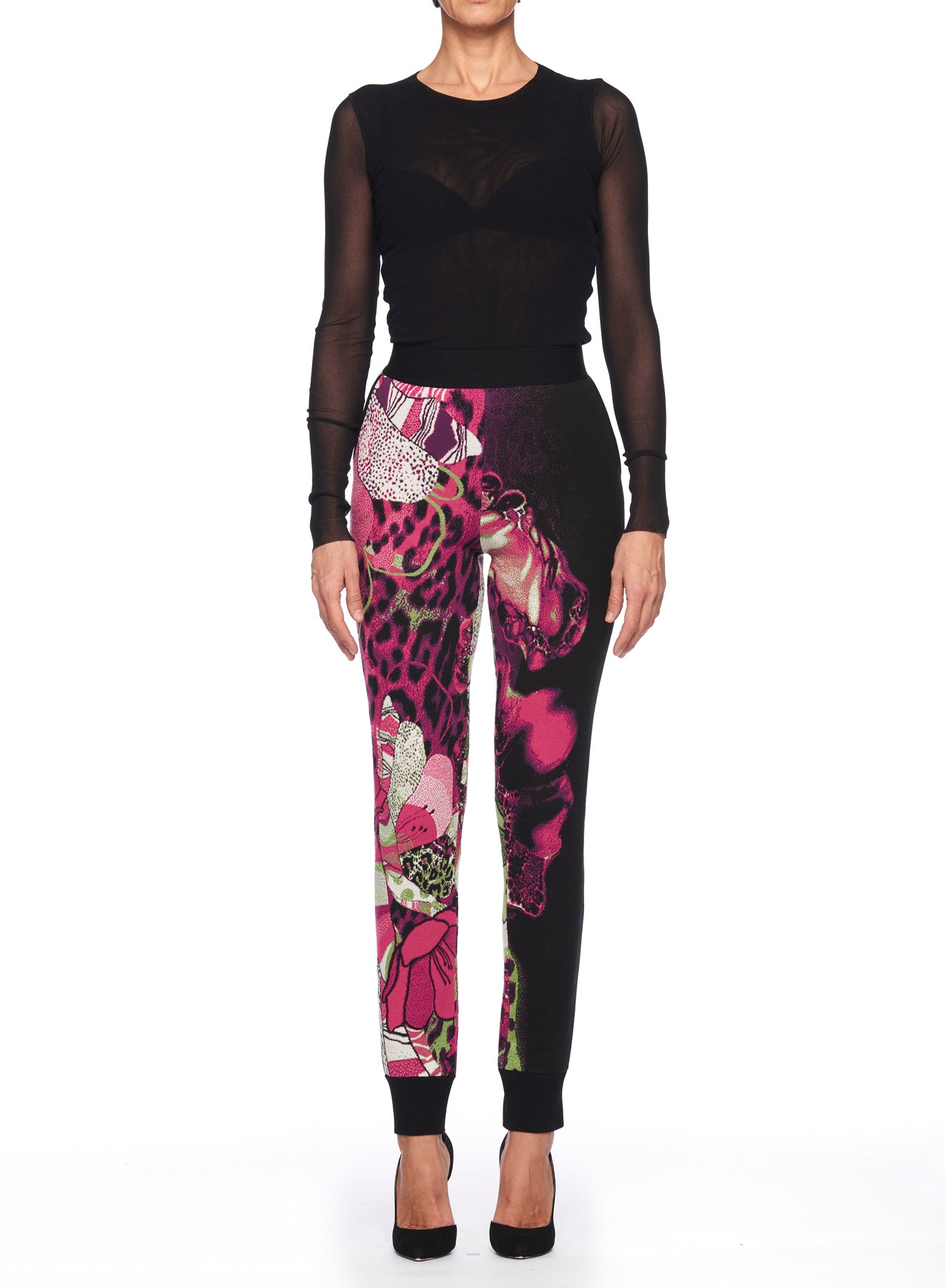 A person wearing a sheer black long-sleeve top and Fuzzi Woman Wild Side Joggers, featuring a mixed print of floral and leopard patterns, stands against a white background. They are also wearing black high-heeled shoes.