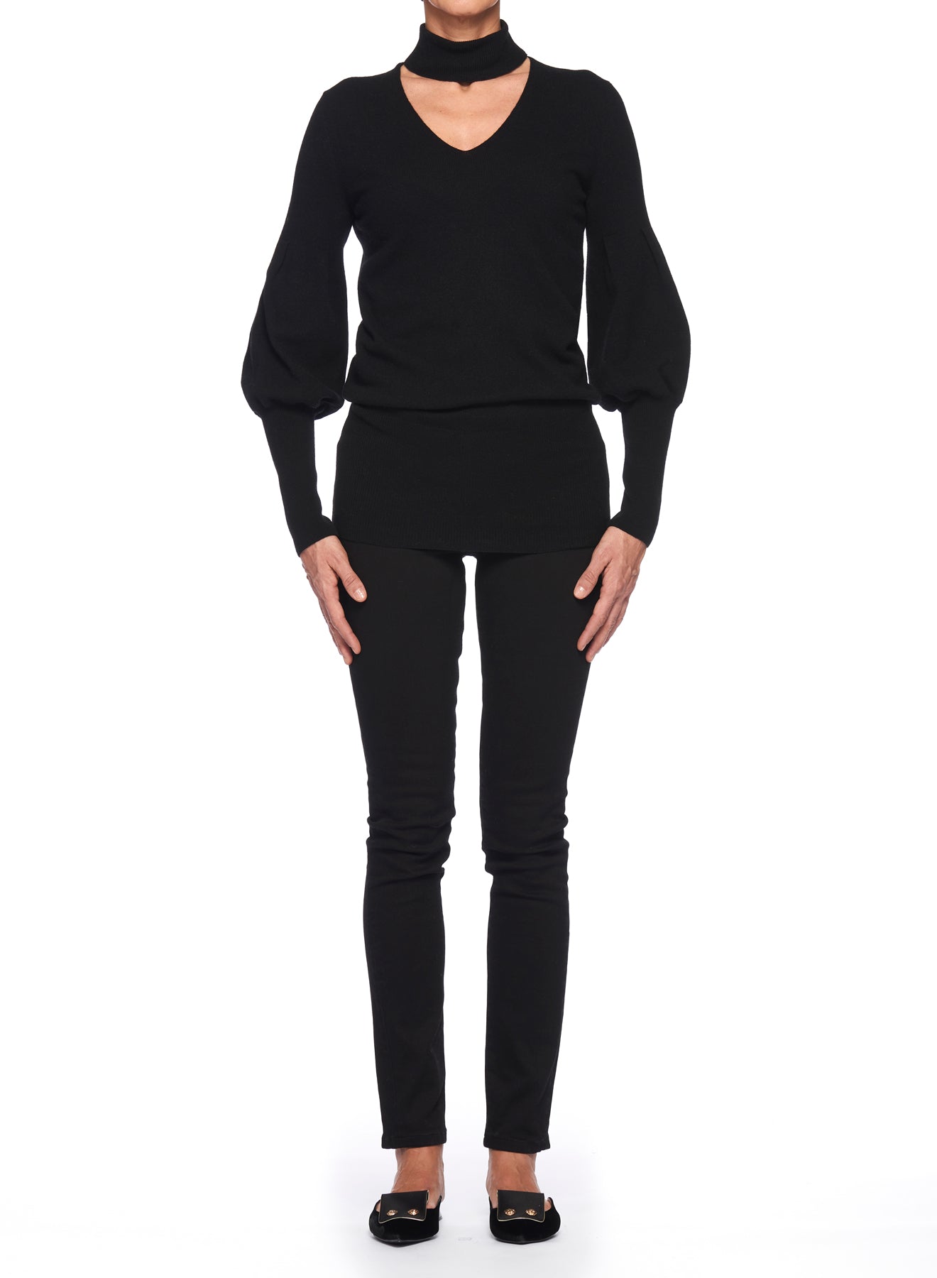 A person stands against a white background wearing the Fuzzi Woman Black V-Neck Sweater with Puff Sleeves, paired with black pants and black shoes. The minimalist outfit is elegantly monochromatic.