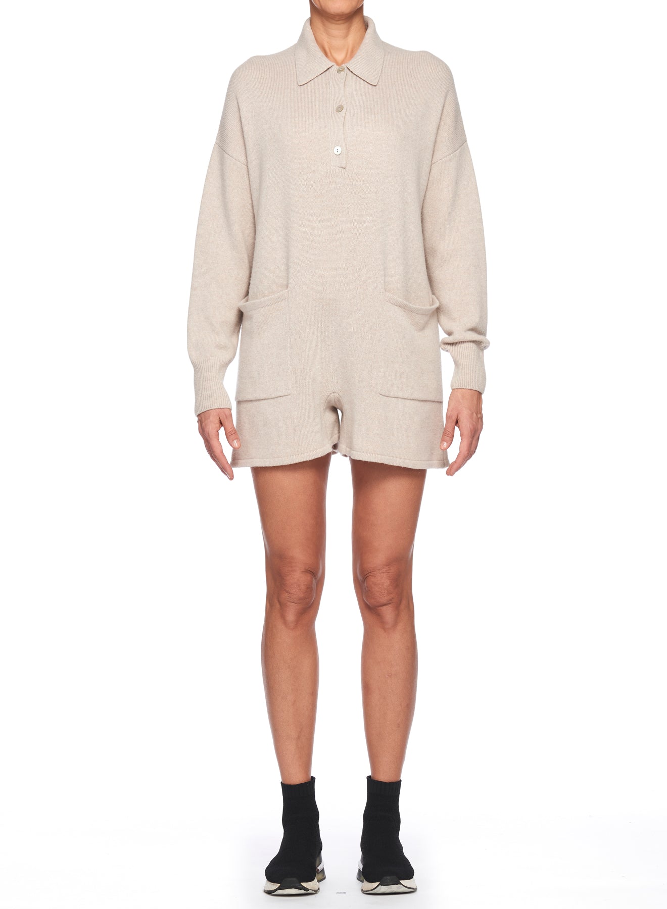 A person is wearing a Fuzzi woman beige polo-neck knit jumpsuit. This chic jumpsuit, featuring front pockets, is paired with black ankle socks and sneakers. The plain white background highlights the timeless style of this ensemble.