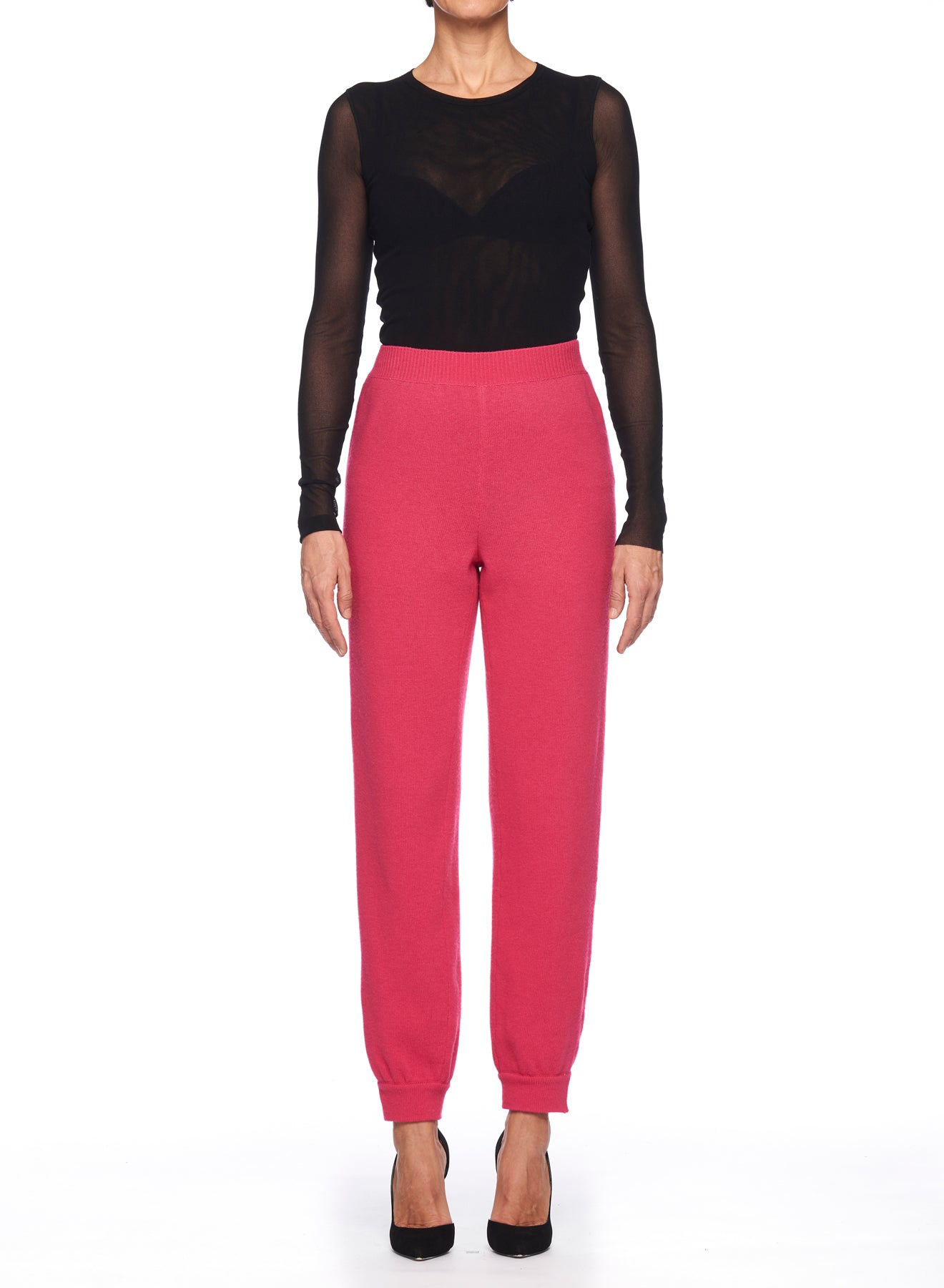 A person wearing a black long-sleeve mesh top and the Fuzzi Woman Pink Knit Joggers stands against a white background. They're also sporting black high-heeled shoes, adding a modern touch to this vintage-inspired piece.