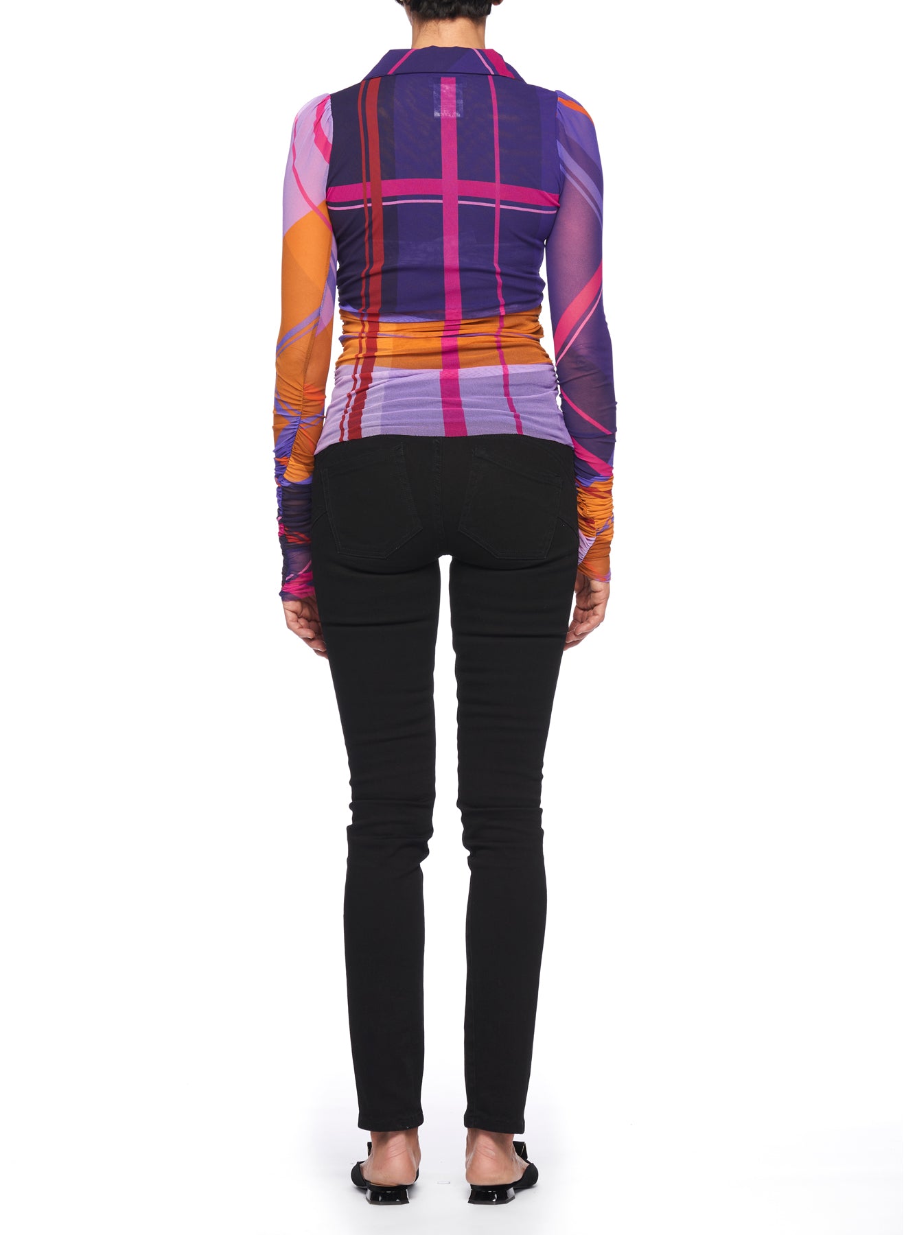 A person stands facing away, wearing the Fuzzi Woman Mesh Top with a vibrant geometric pattern in shades of purple, pink, and orange. They pair it with black pants and black shoes against a white background.