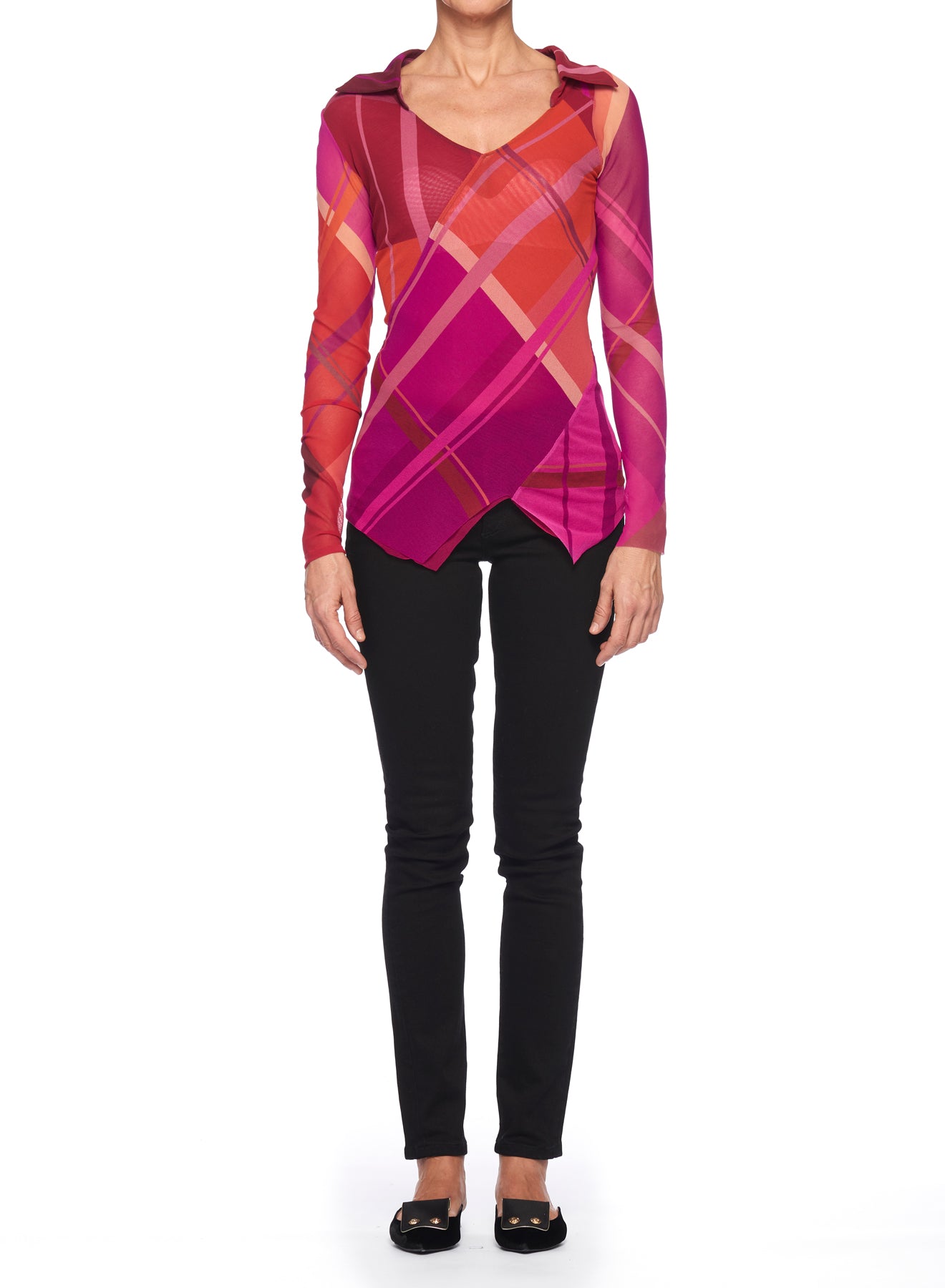 A person stands against a white background wearing the Fuzzi Woman Colorful Mesh Blouse by Fuzzi, featuring vibrant red and pink diagonal stripes with an abstract print. The mesh top has an asymmetrical hem and a scoop neckline, paired with black pants and black shoes.