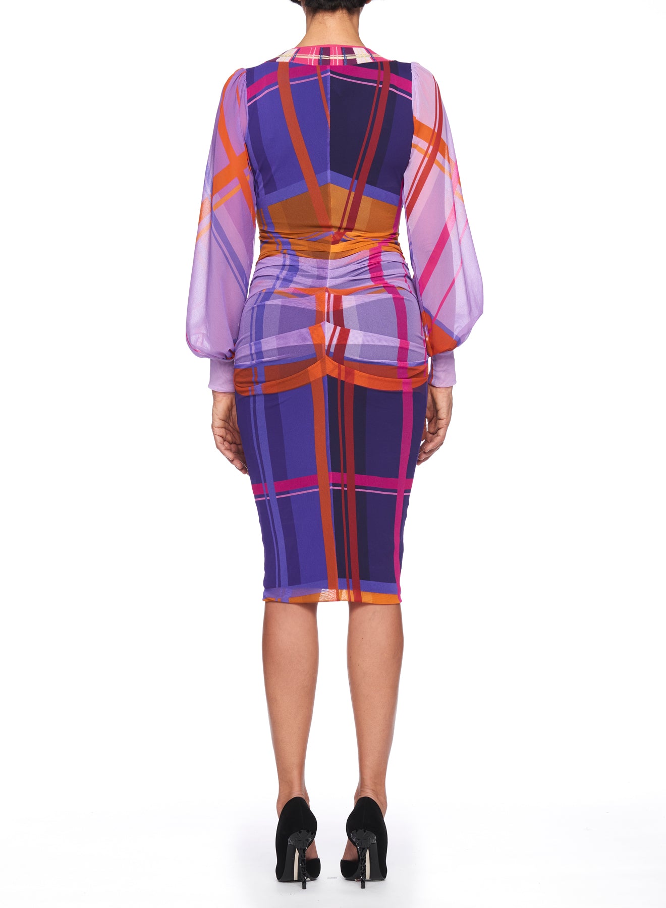 A person wearing the Fuzzi Woman Colorful Dress with a bold vintage plaid pattern in purple, pink, and orange shades. The dress by Fuzzi features sheer long sleeves and a knee-length hem. They stand with their back to the camera in black high heels.