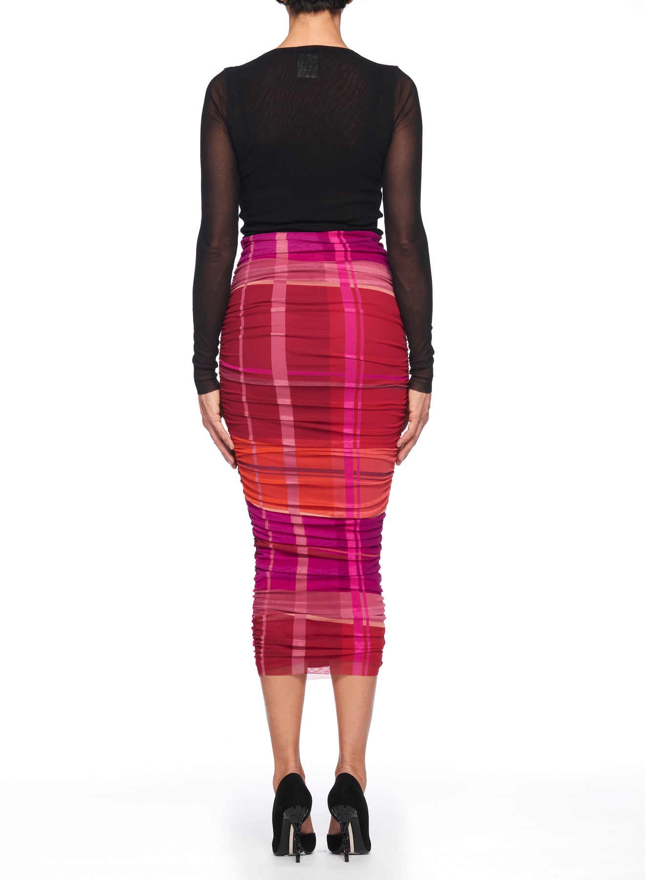 A person wearing a sheer black long-sleeve top and the Fuzzi Woman Multicolor Midi Skirt featuring a ruched design stands facing away, accompanied by black high heels. The setting is a plain white background.