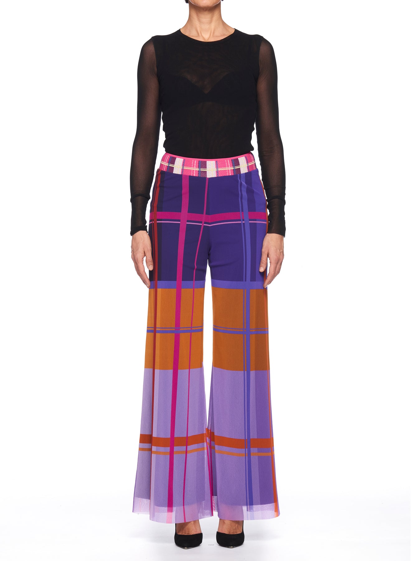 A person is dressed in a black sheer long-sleeve top paired with Fuzzi Woman Colorful Wide-Leg Pants by Fuzzi, showcasing a vivid plaid design in bold purple, pink, orange, and white tones. The look is finished with black heels against a plain white backdrop.