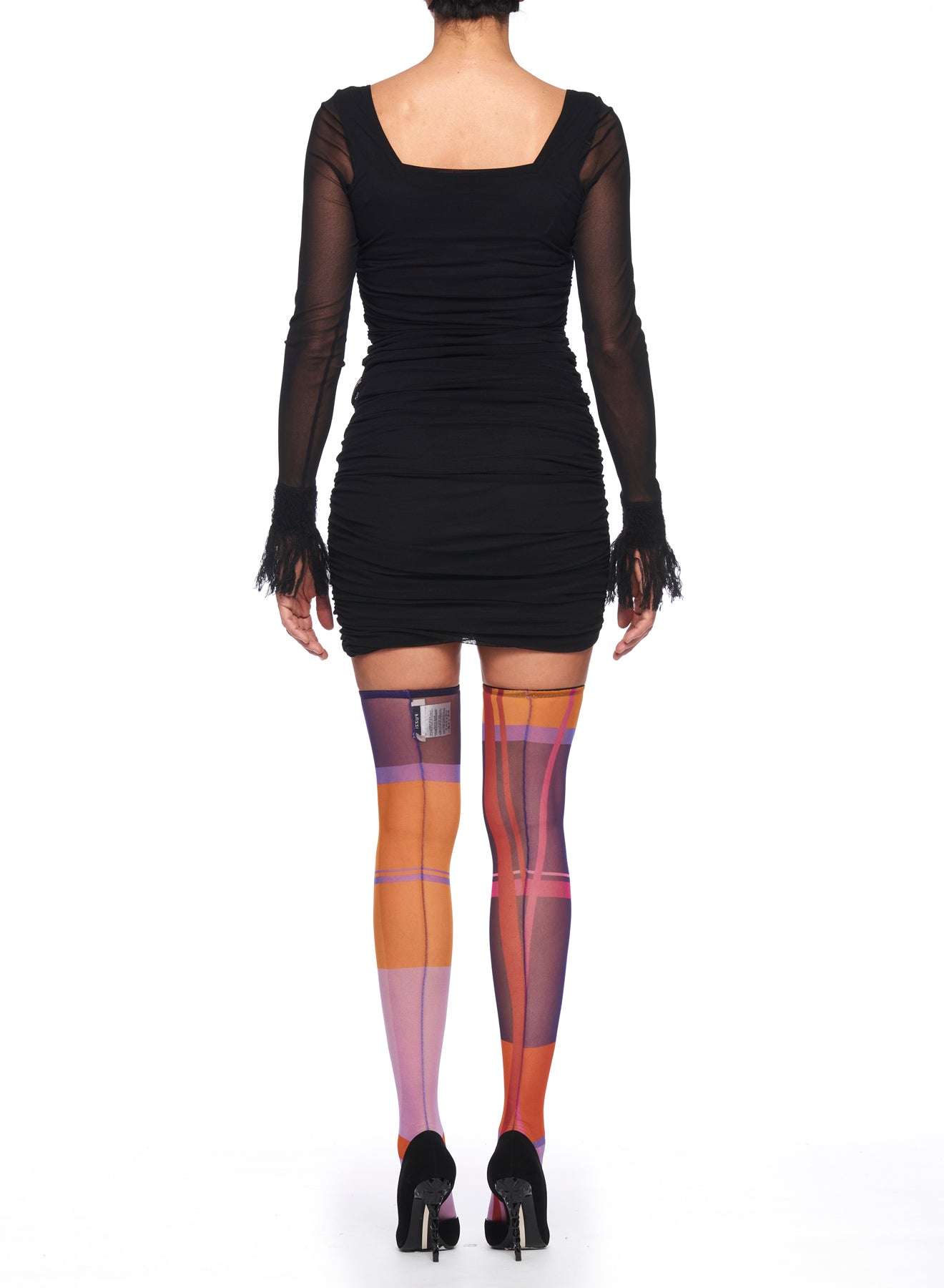 A person wearing a fitted black dress with sheer sleeves stands facing away. Their Fuzzi Woman Colorful Tights by Fuzzi, featuring an abstract print in shades of pink, orange, and purple, serve as a striking statement piece, perfectly paired with black ankle-strap heels.