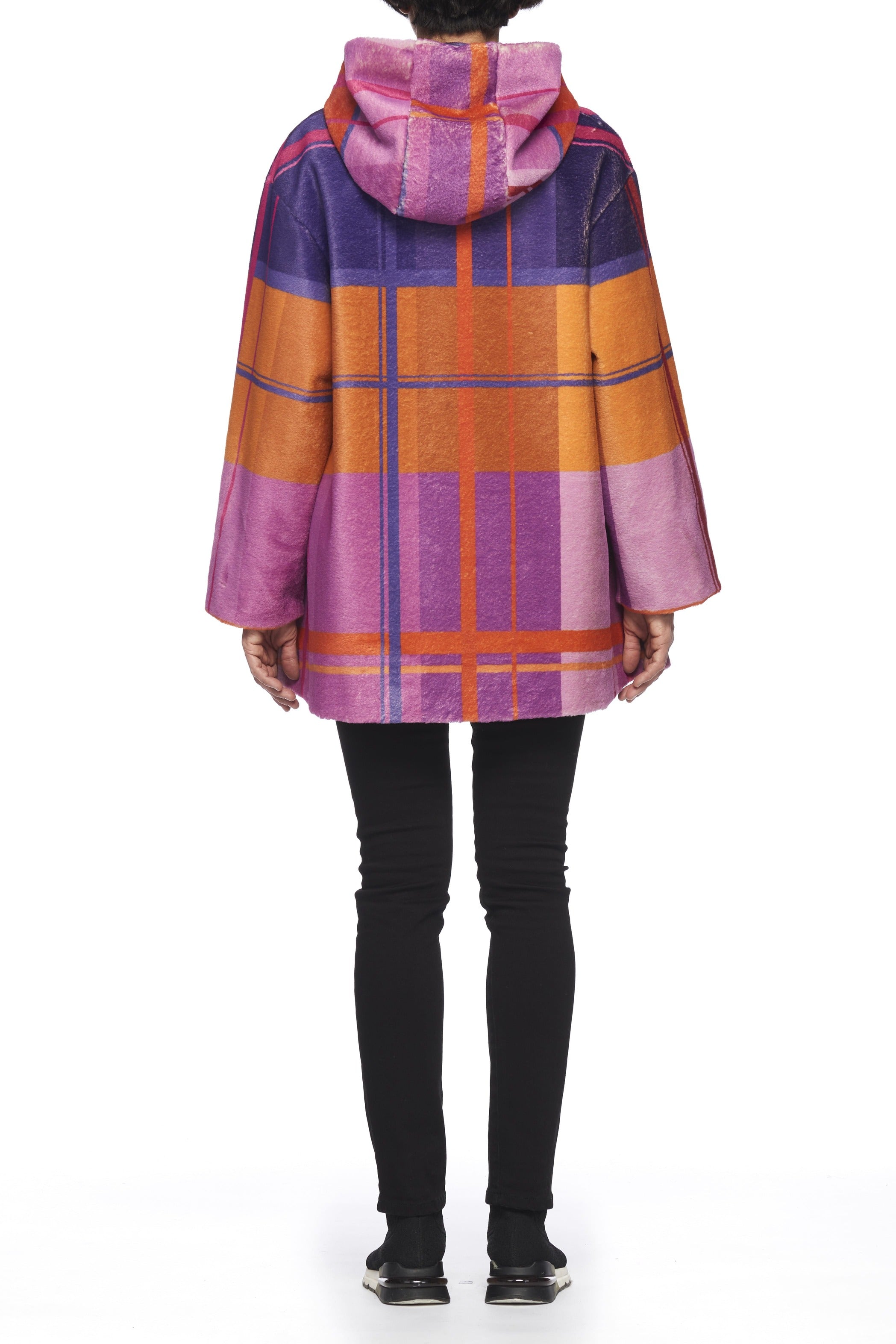 A person stands with their back to the camera, wearing the Fuzzi Woman Colorful Oversized Coat by Fuzzi, showcasing a vibrant plaid pattern in shades of pink, purple, orange, and red. The hooded coat perfectly complements black pants and shoes.