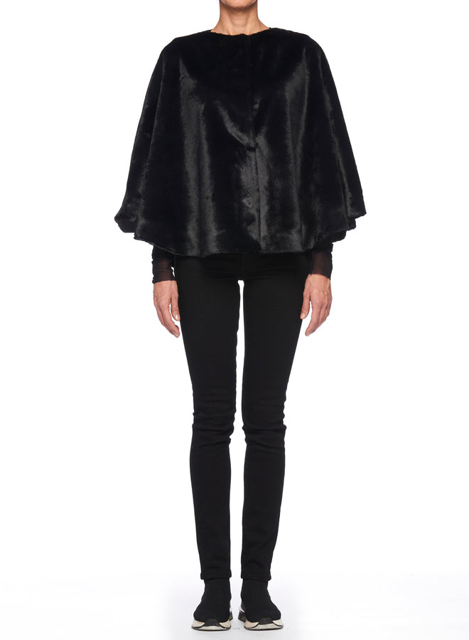 A person wearing the Fuzzi Woman Black Cape Coat from Fuzzi over a black outfit stands against a white background. The vintage piece drapes elegantly in a loose fit, while the black pants and shoes complete the monochrome look.