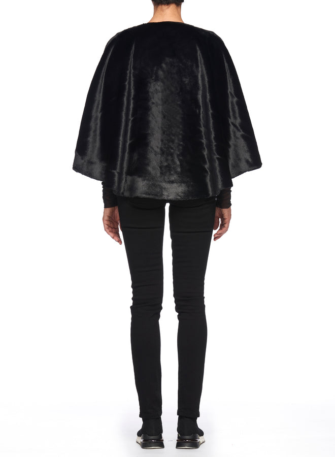 A person dressed in black pants, shoes, and a long-sleeve top is shown from behind, highlighting a vintage piece—the luxurious Fuzzi Woman Black Cape Coat—set against a plain white background.