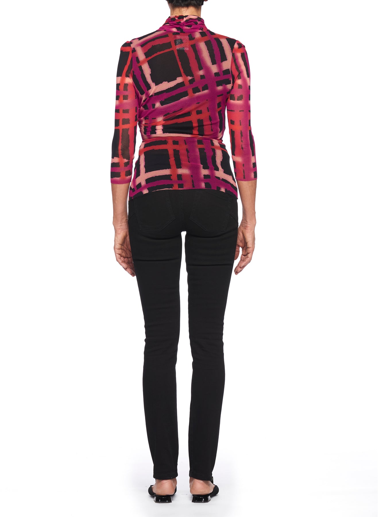 A person stands with their back to the camera, wearing a vibrant Fuzzi Woman Abstract Print Top with Tie Waist in shades of pink, red, and black that exudes a vintage piece charm. They are also wearing black pants and shoes against a plain white background.