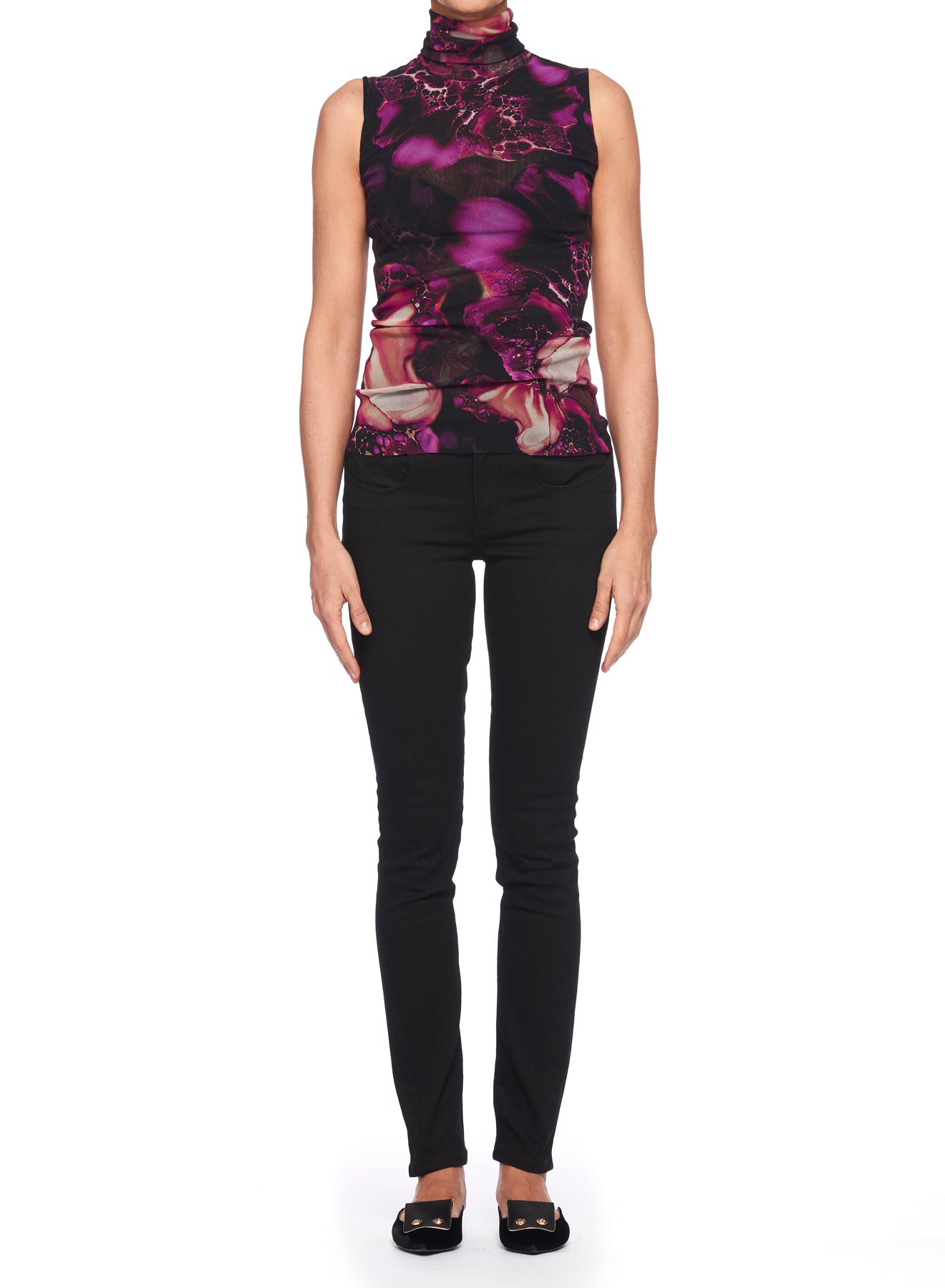 A person stands against a white background, dressed in the Fuzzi Woman Top with a sleeveless design featuring a purple and black abstract print, paired with black pants and shoes. Their arms rest comfortably at their sides.