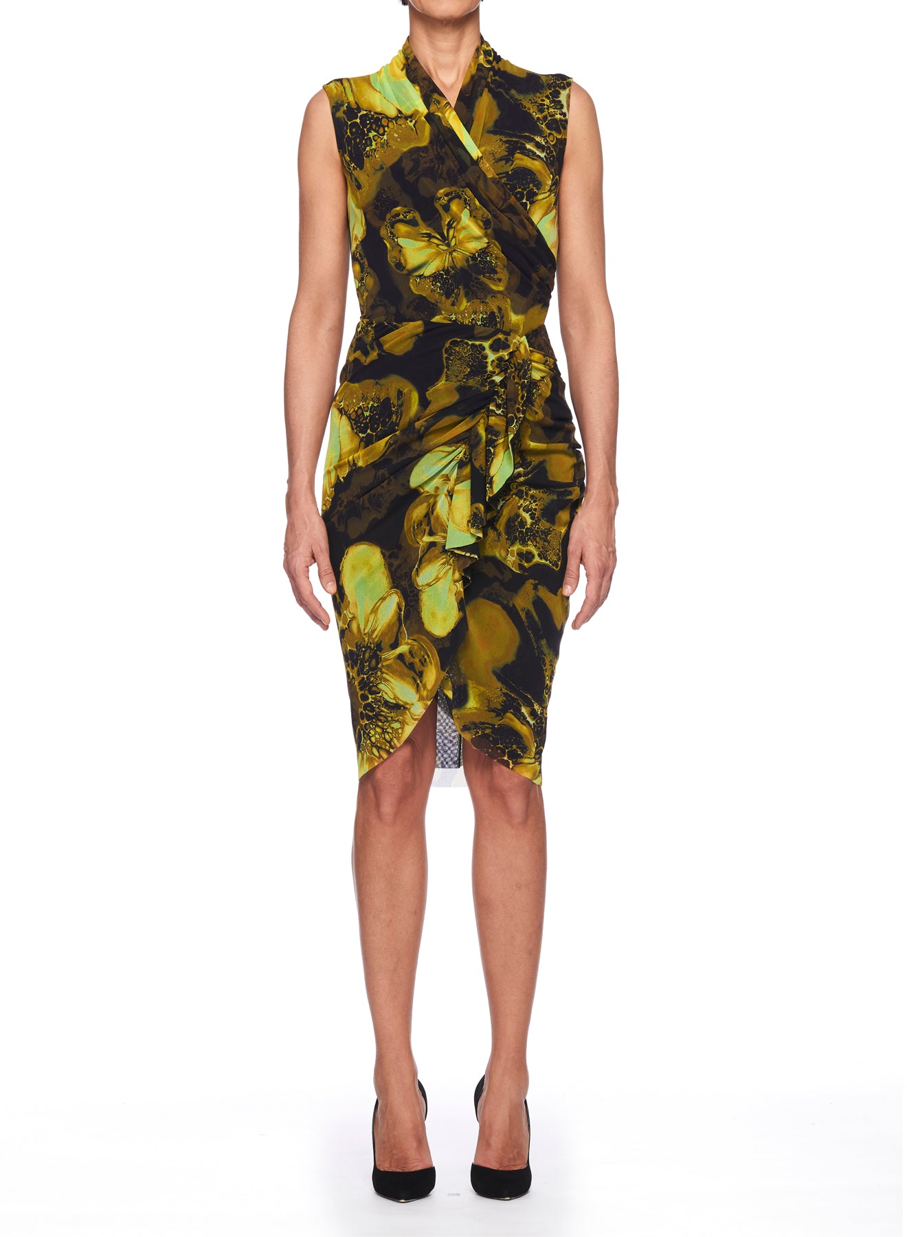 A person wearing the Fuzzi Woman Wrap Dress from Fuzzi, featuring a vibrant yellow and black floral pattern, stands against a white background. The dress, known for its striking wrapped design, is complemented by black high heels.