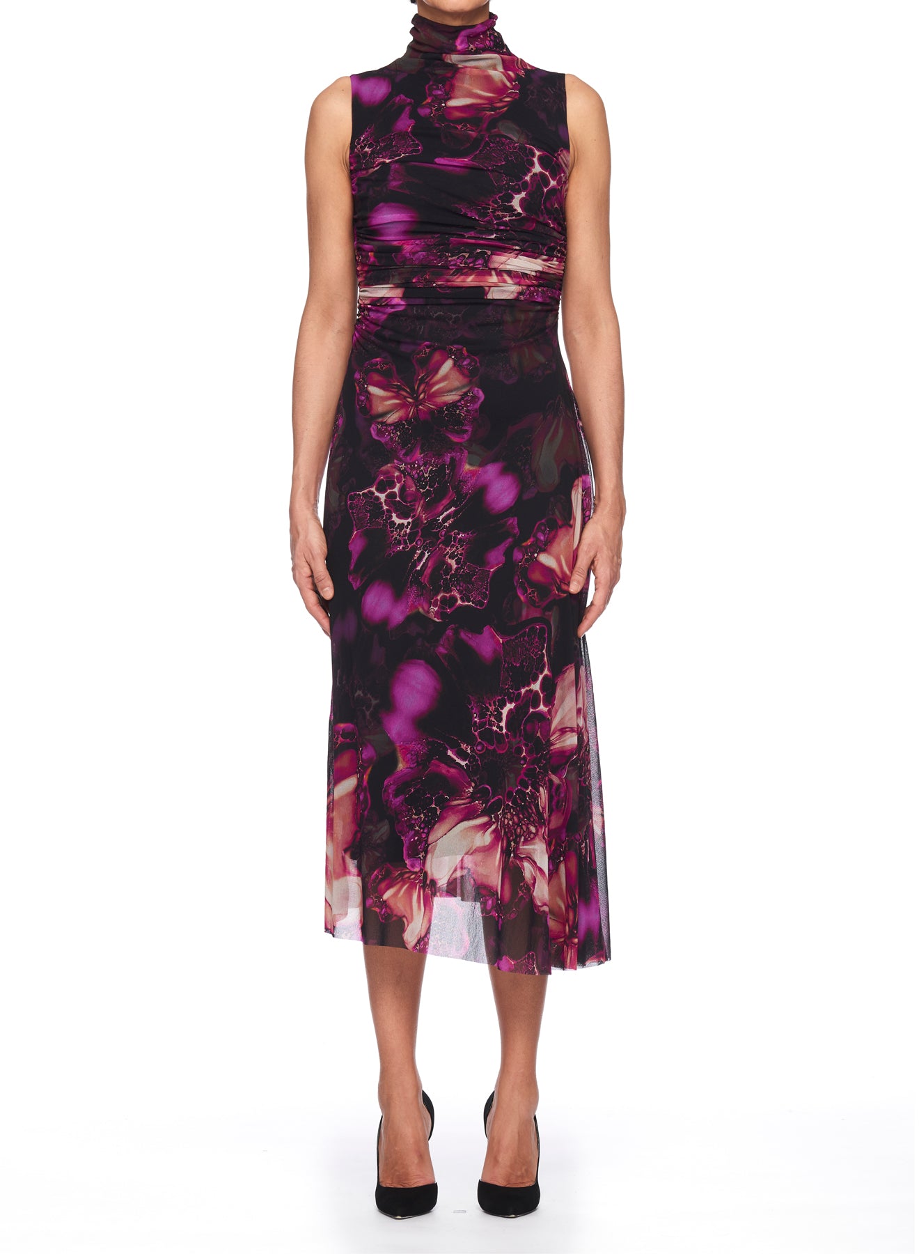 A person stands on a white background wearing the Fuzzi Woman Mesh Dress with High Neck by Fuzzi, which features a vibrant purple and pink floral pattern reminiscent of an abstract print, paired with black heels.