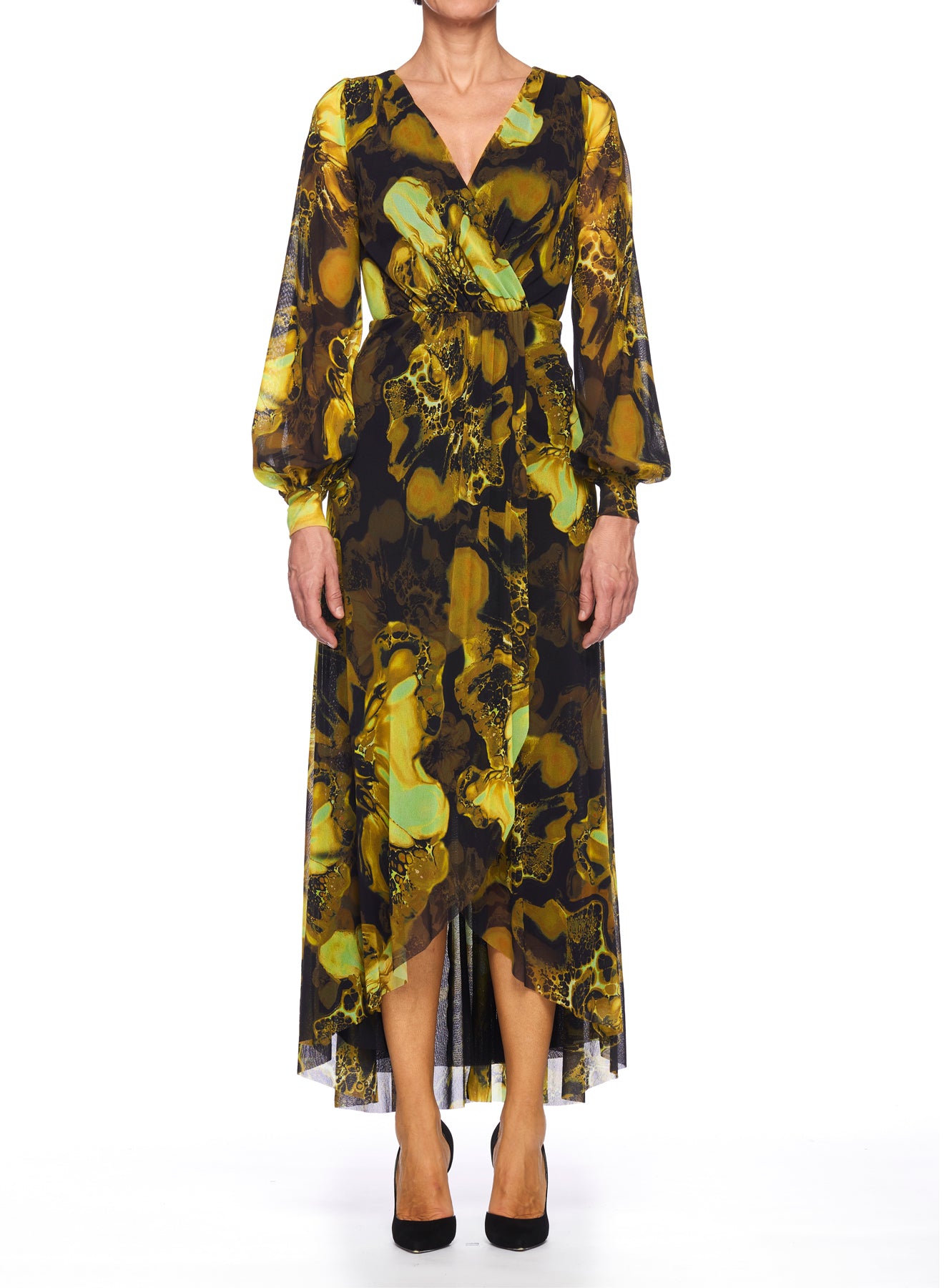 A person wearing the Fuzzi Woman Dress with Floral Pattern stands against a white background. This vintage-inspired dress by Fuzzi features a long, flowy wrap design with a yellow and green abstract floral pattern, complemented by long sleeves and a V-neckline. The outfit is perfectly completed with black shoes.