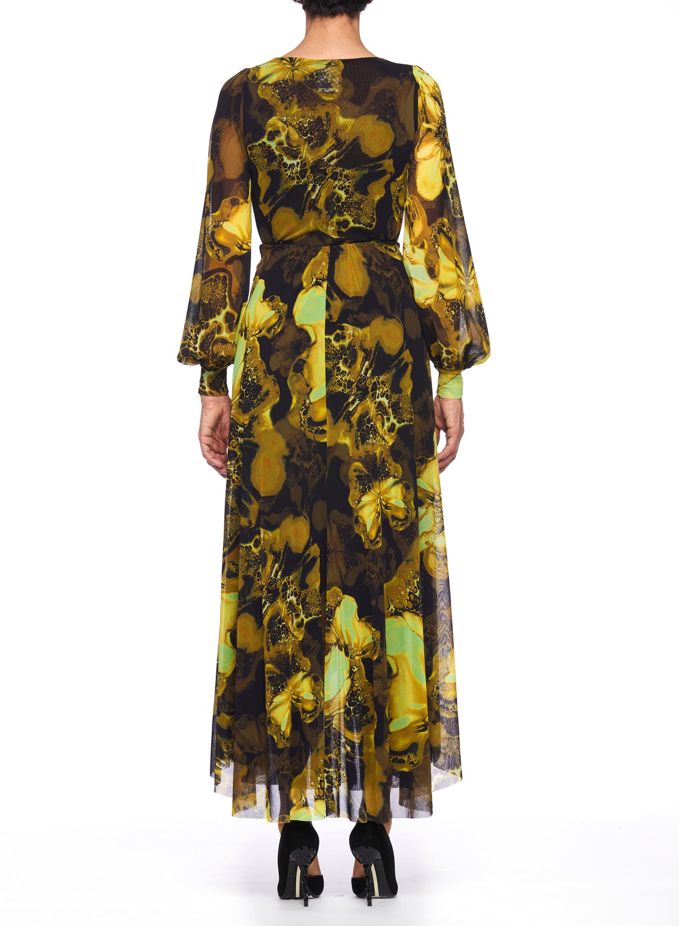 Wearing a vintage piece from Fuzzi, the individual dons a Fuzzi Woman Dress with a striking yellow and black abstract floral pattern. This wrap dress, featuring sheer long sleeves, is beautifully paired with black high-heeled shoes as they stand facing away.