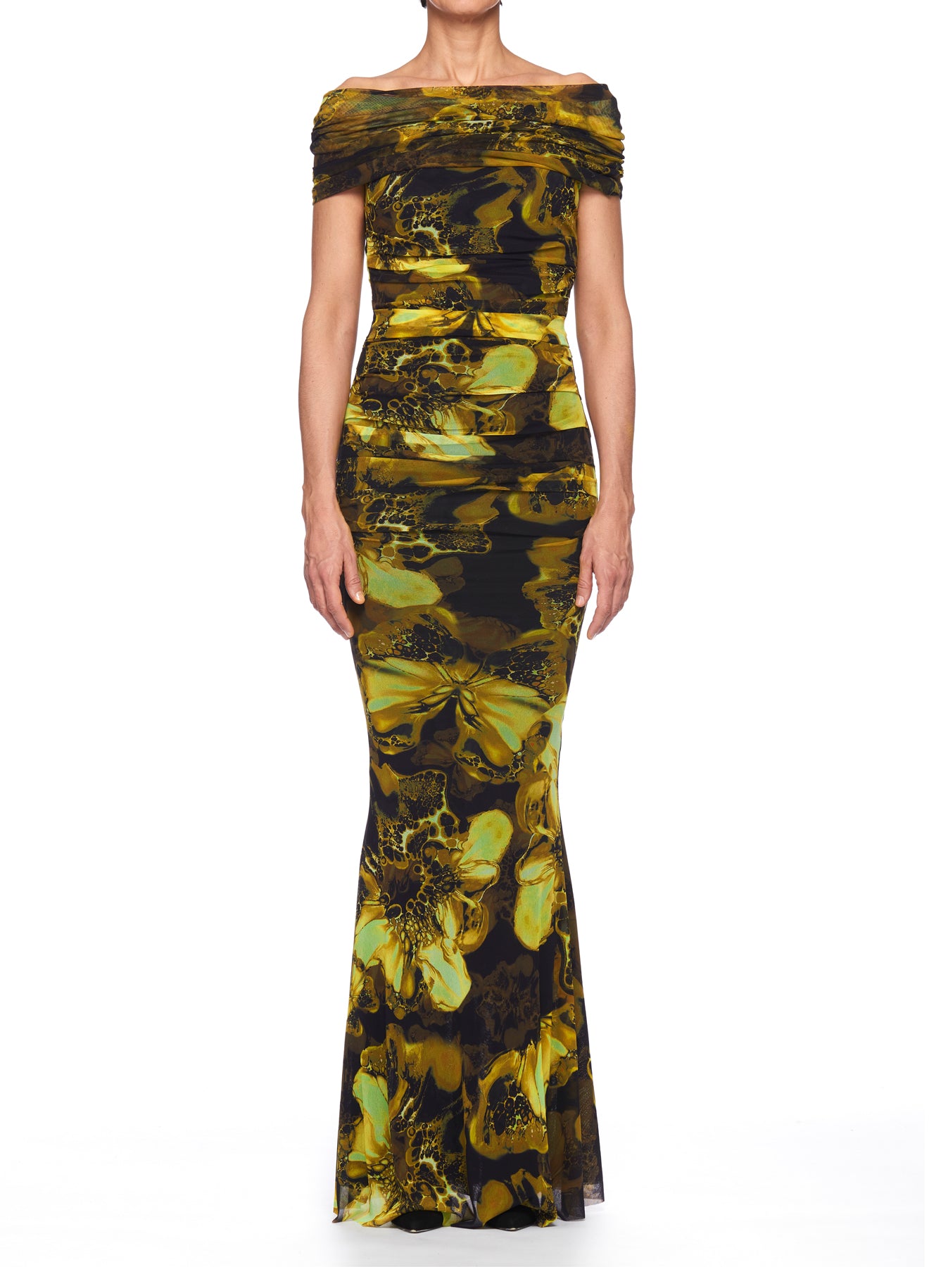 A person stands against a plain white background wearing the Fuzzi Woman Maxi Dress with Mermaid Silhouette, a fitted off-the-shoulder gown by Fuzzi that features an elegant contemporary design with a yellow and black abstract pattern.