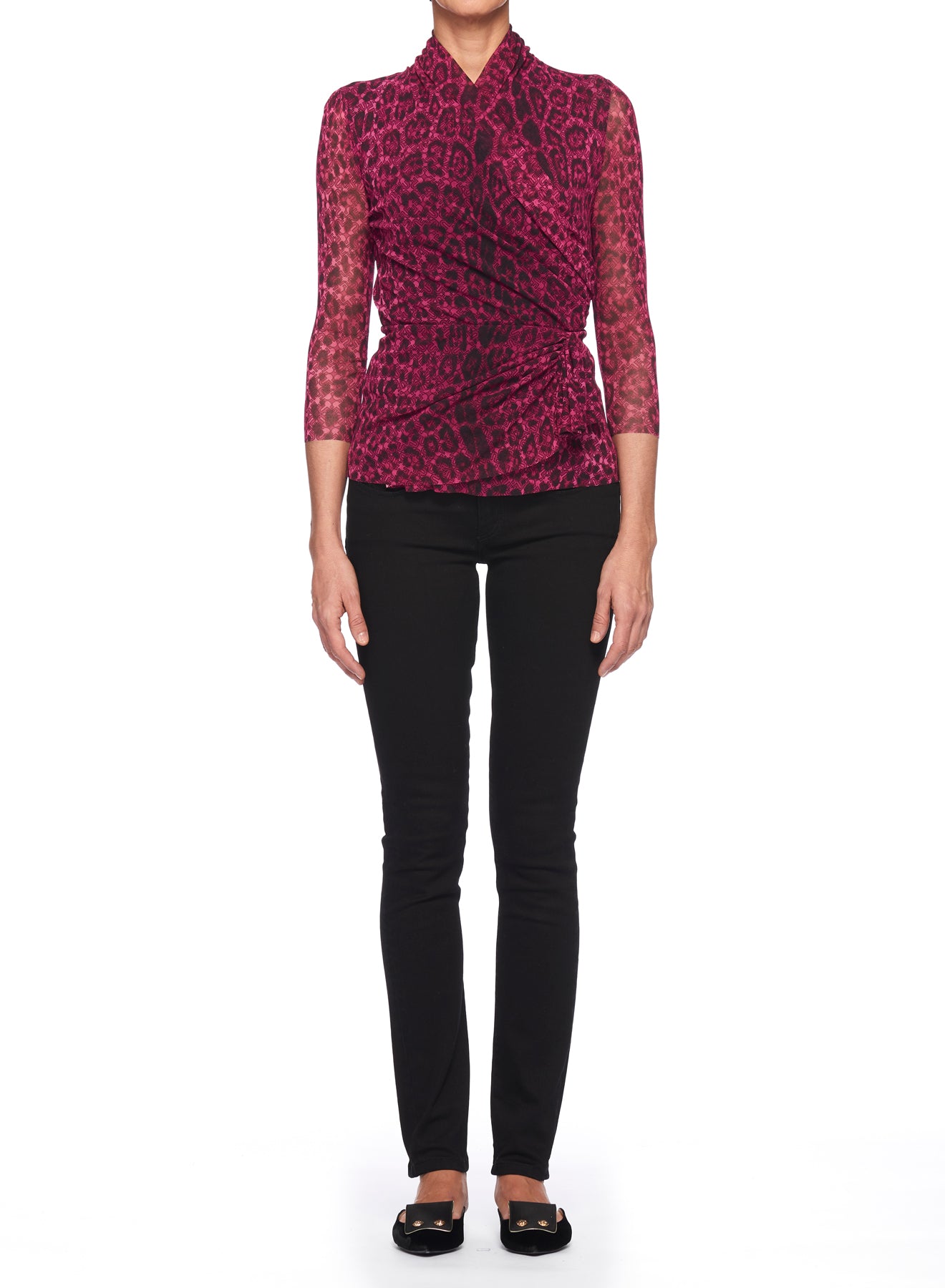 A person poses against a white background wearing the Fuzzi Woman Leopard Print Mesh Top with High Neck in vibrant pink and black, paired with sleek black pants and classic flat shoes. Their arms are relaxed at their sides, exuding effortless style.