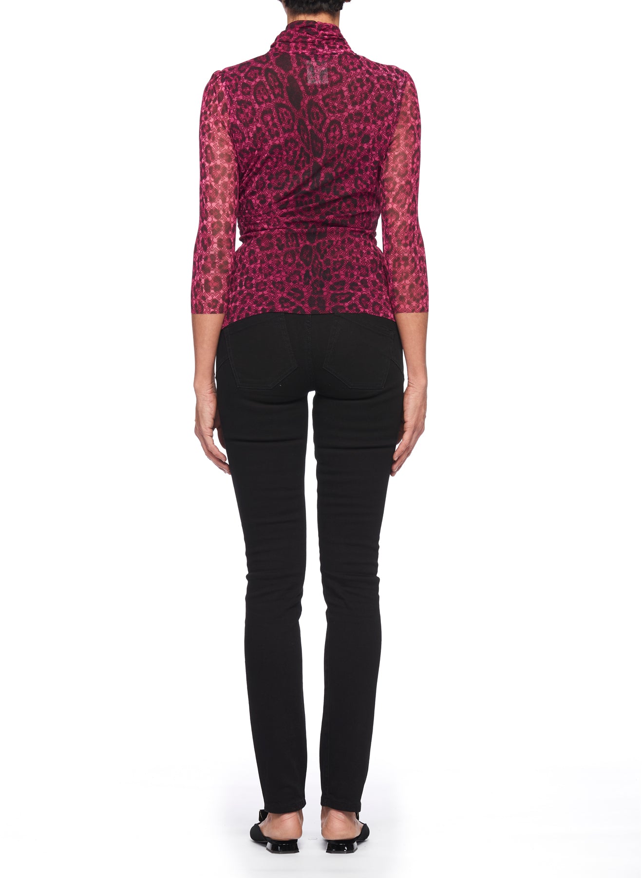 Rear view of a person wearing the Fuzzi Woman Leopard Print Mesh Top with a high neck, paired with black jeans. They are standing against a plain white background.